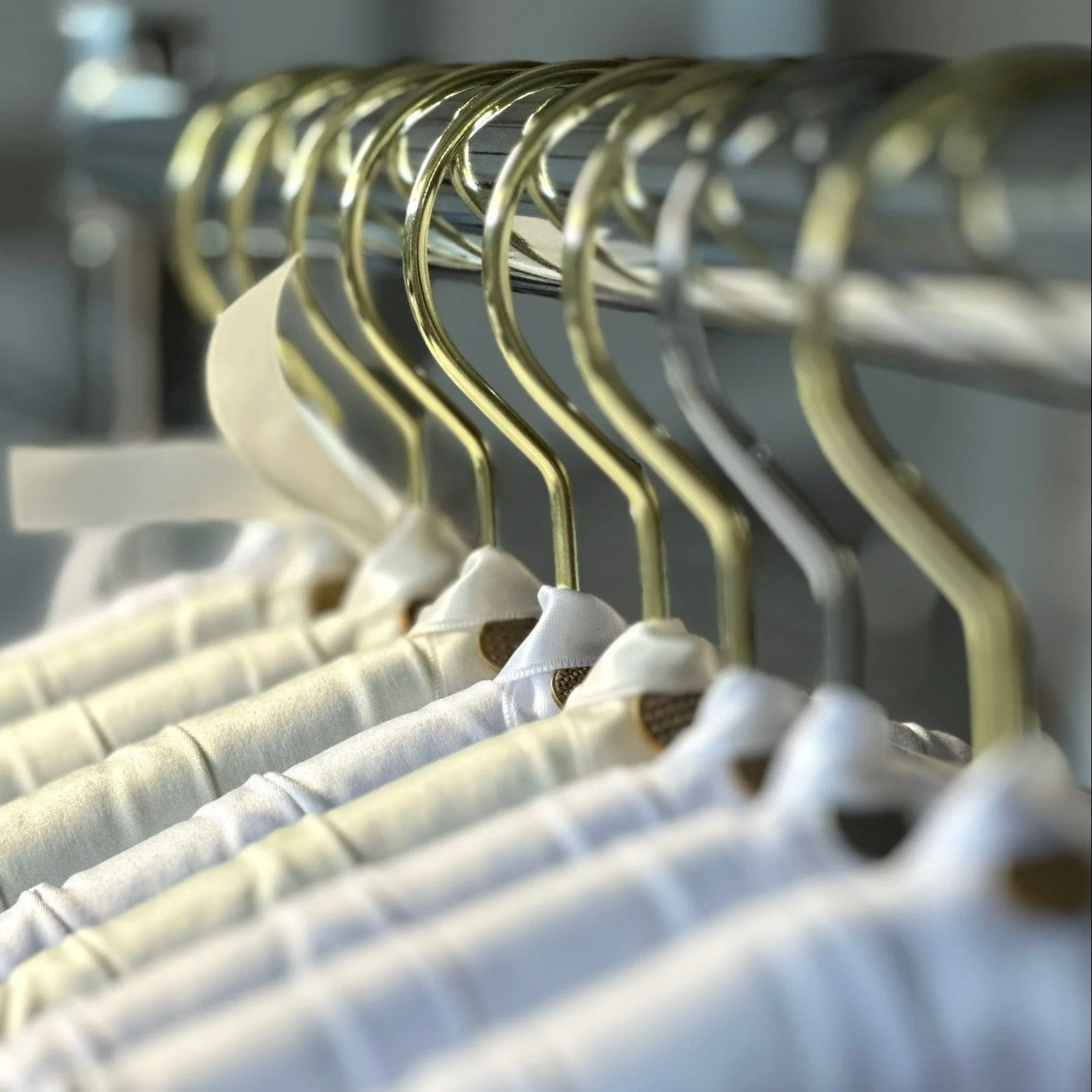 rows of ivory and white personalized satin bridal hangers being made. Luxe satin bridal hangers feature a small gold or silver charm on the back of each hanger, as pictured here.