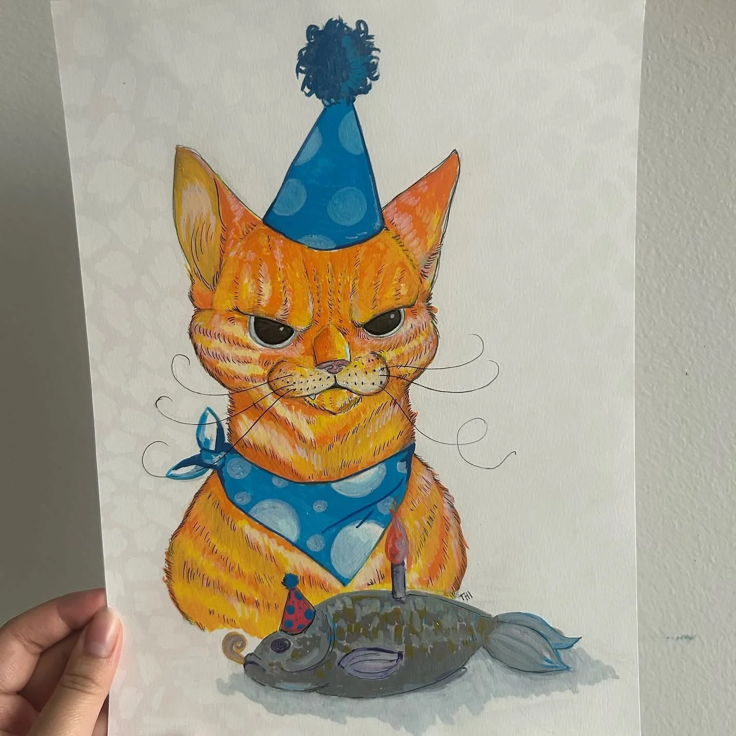 Illustration of an orange tabby cat wearing a blue birthday hat with pom-pom, a blue polka-dot bandana, and a red birthday hat with blue dots. The cat has a grumpy expression, sitting beside a fish with a candle on its back, indicating a birthday cel