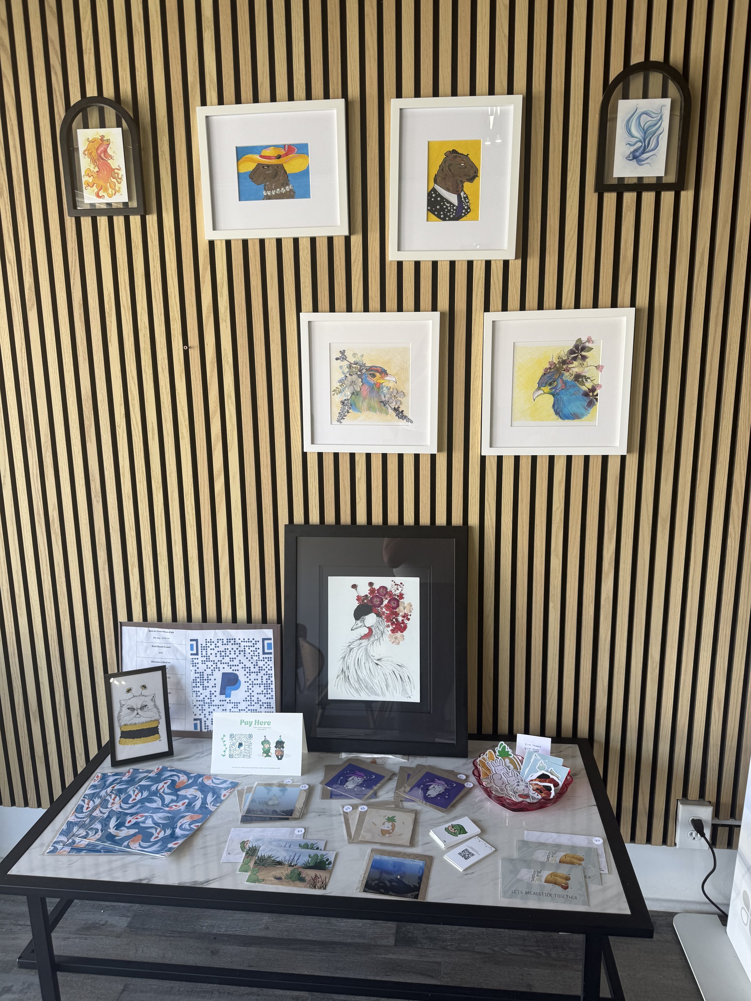 Display of colorful artwork featuring animals and abstract designs on a wooden wall and table.