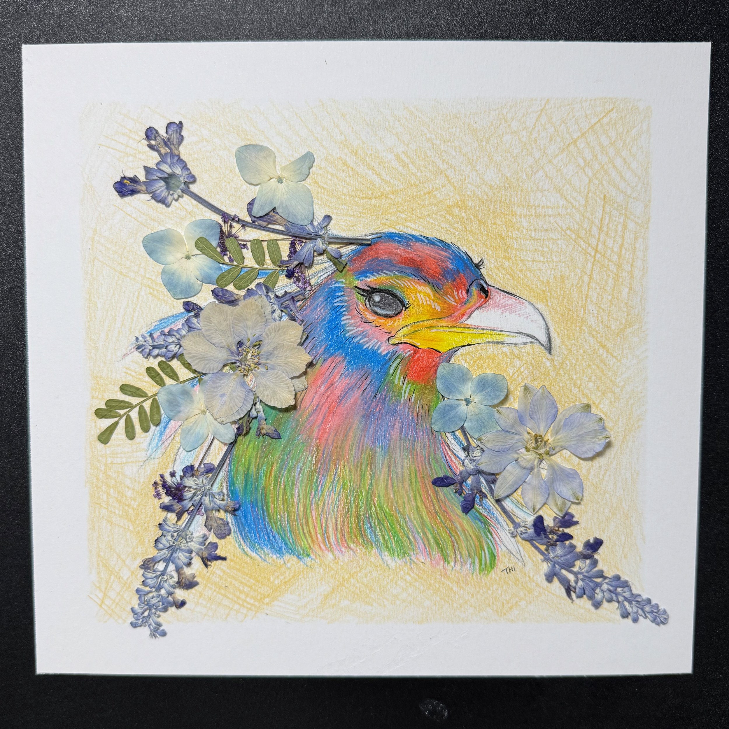 A colorful drawing of an eagle with blue, red, green, and yellow feathers, decorated with real light blue and white flowers against a yellow background.