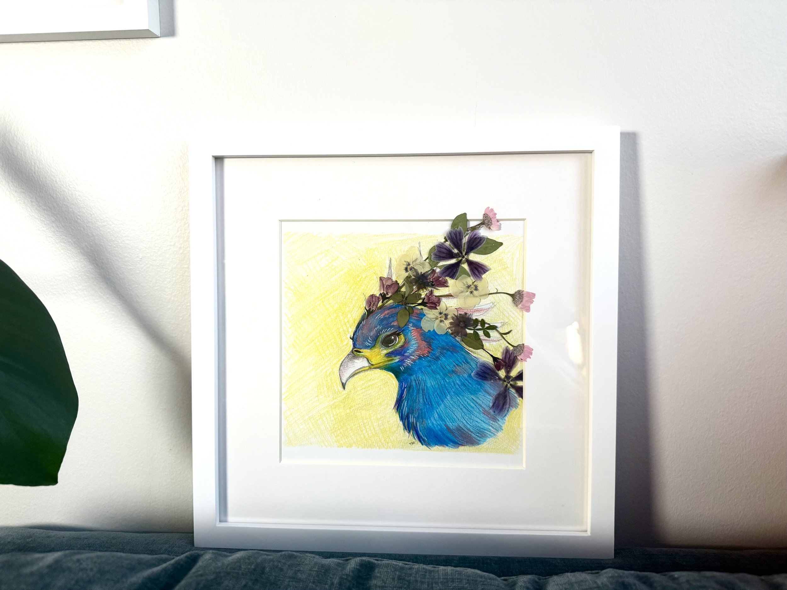 Framed art print of a colorful bird with purple and pink flowers on its head, set against a yellow background.