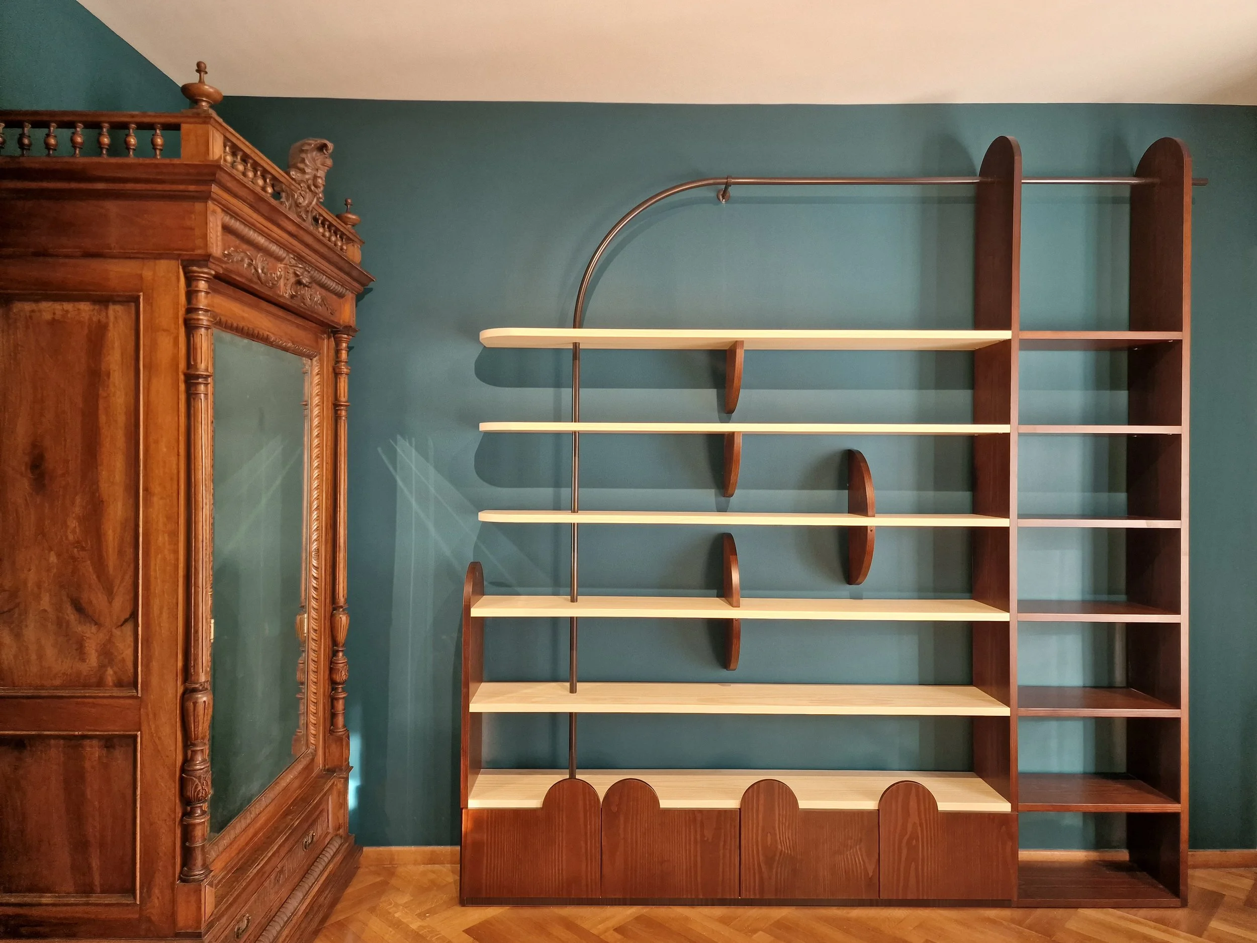 Empty wooden bookshelf against a teal wall, with a vintage wooden cabinet to the left.