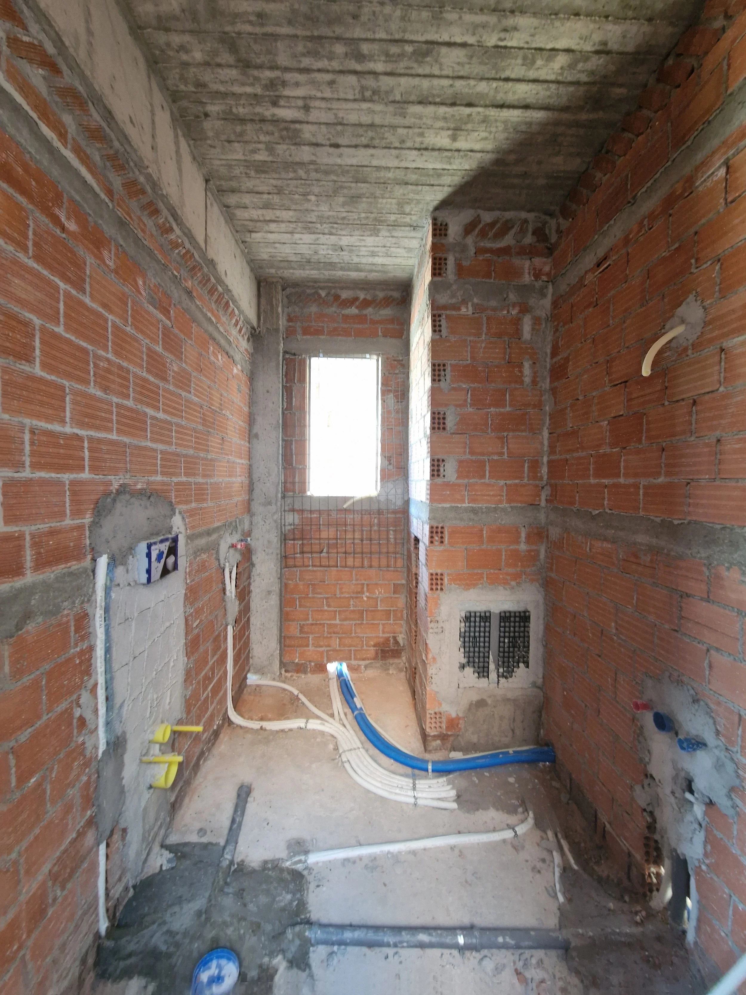 Construction site of an unfinished brick wall room with visible plumbing pipes on the floor.