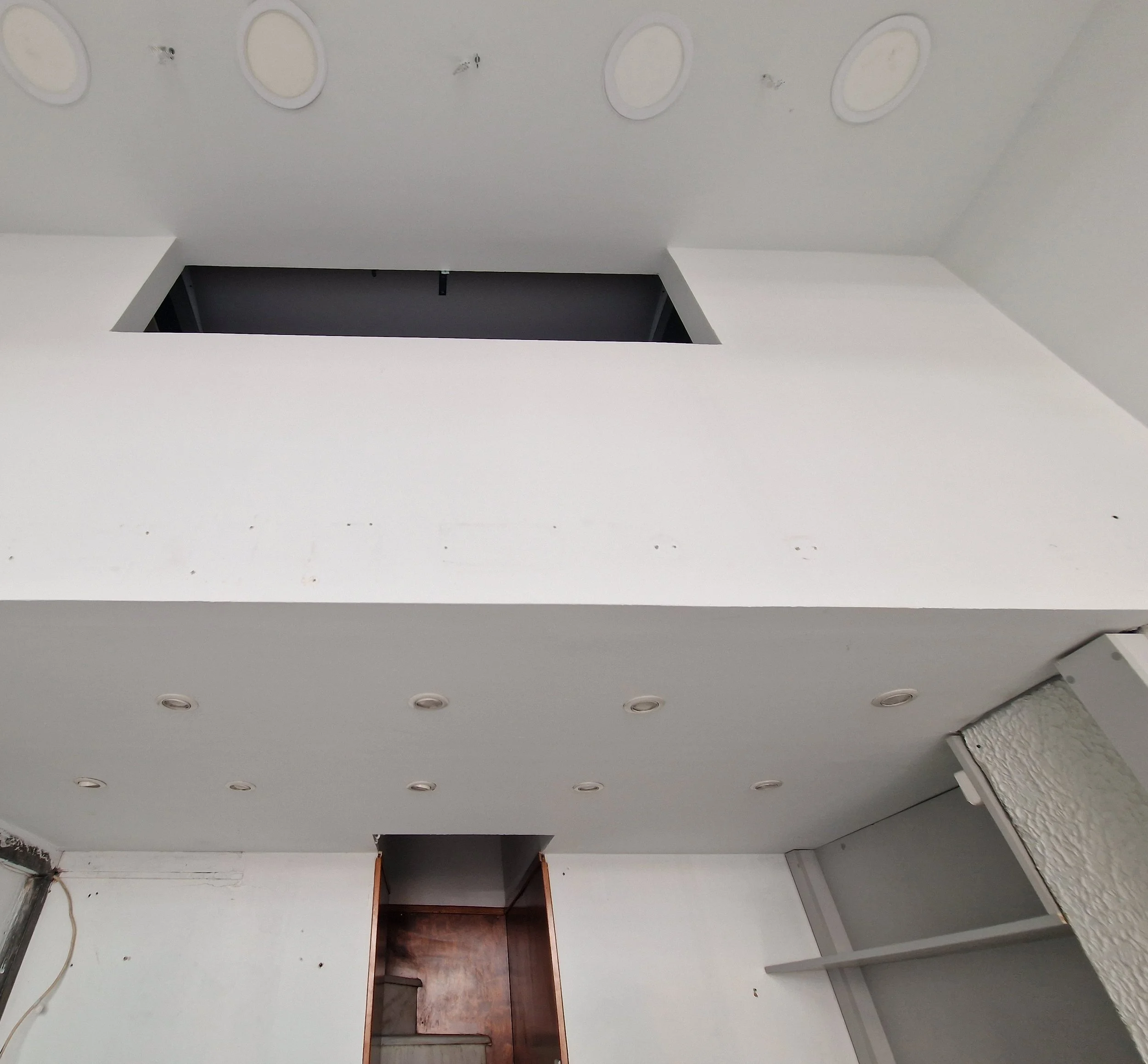 Ceiling with six round recessed lights, two ceiling vents, and an empty bookshelf with a cabinet below.