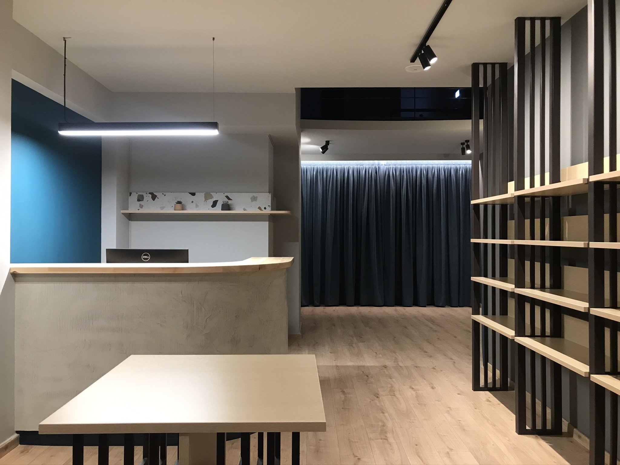 Modern interior space with wooden tables, black structures, blue wall, and ceiling lighting.