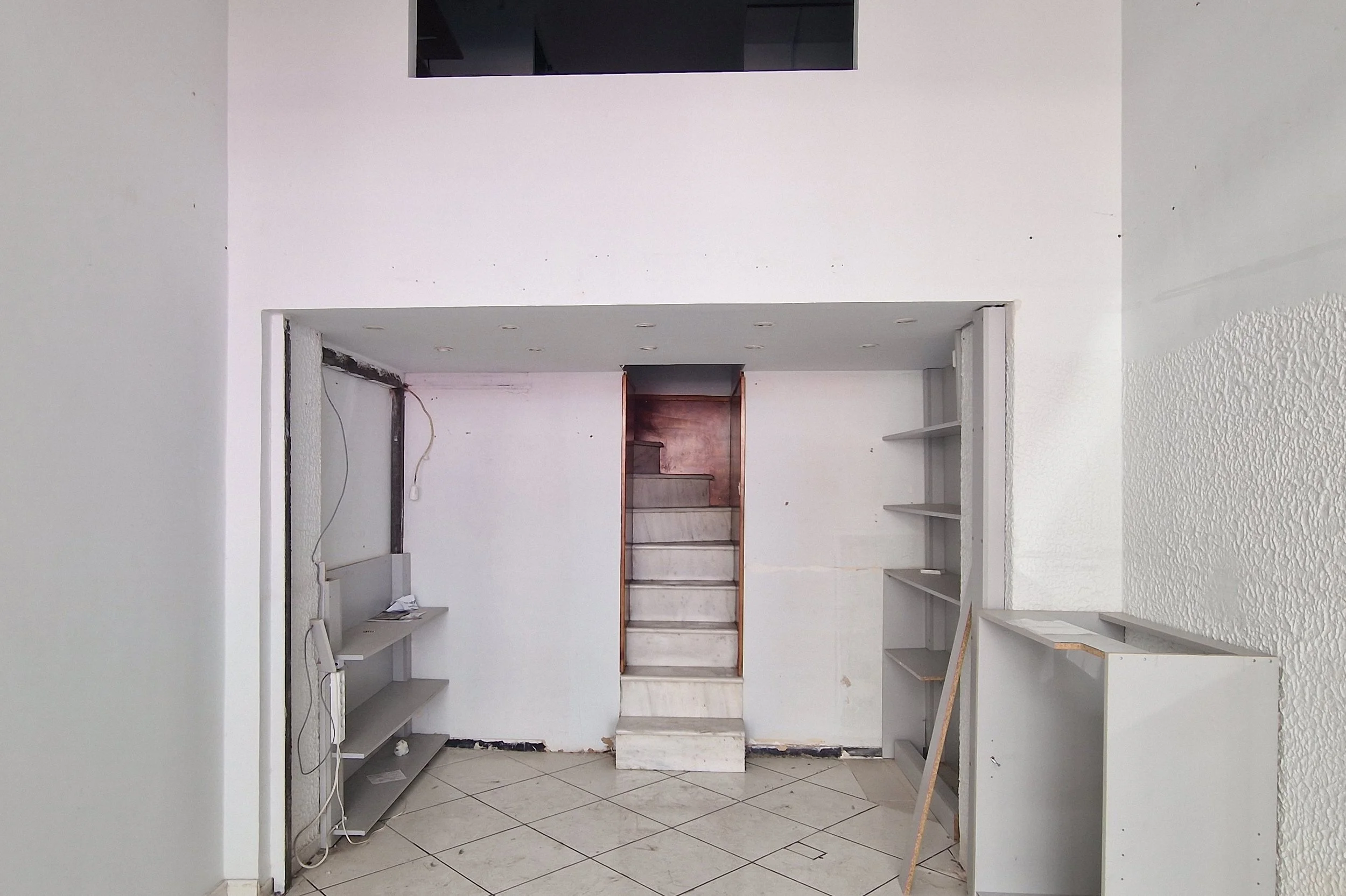 Empty built-in white shelves and cabinetry in a room under construction or renovation with exposed wiring and unfinished surfaces.