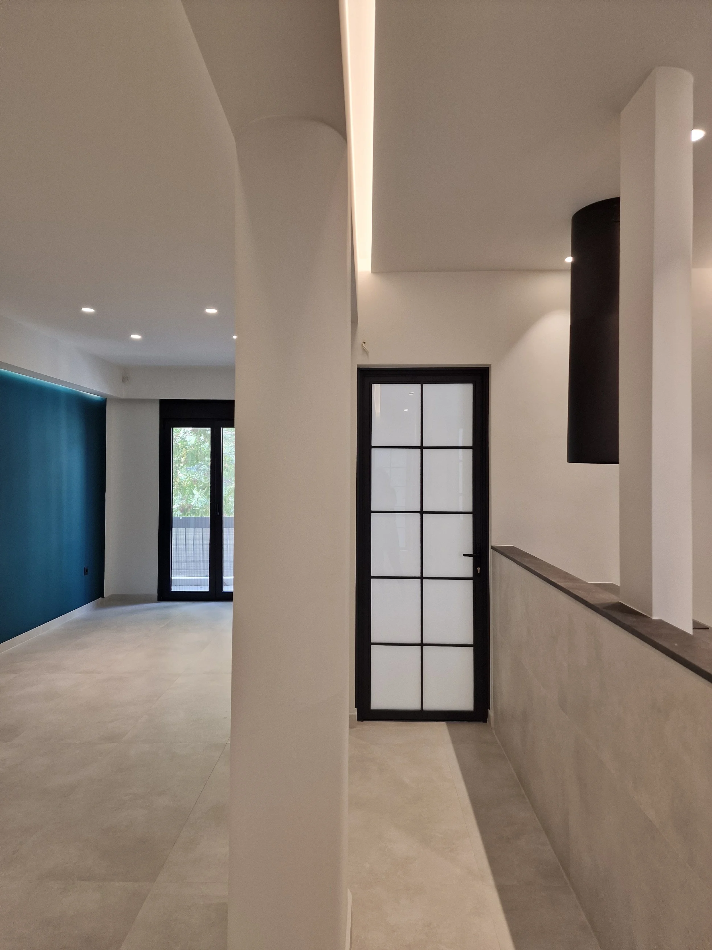 Modern interior space with white walls, beige tiled floor, black-framed window and door, and a white column dividing the room.