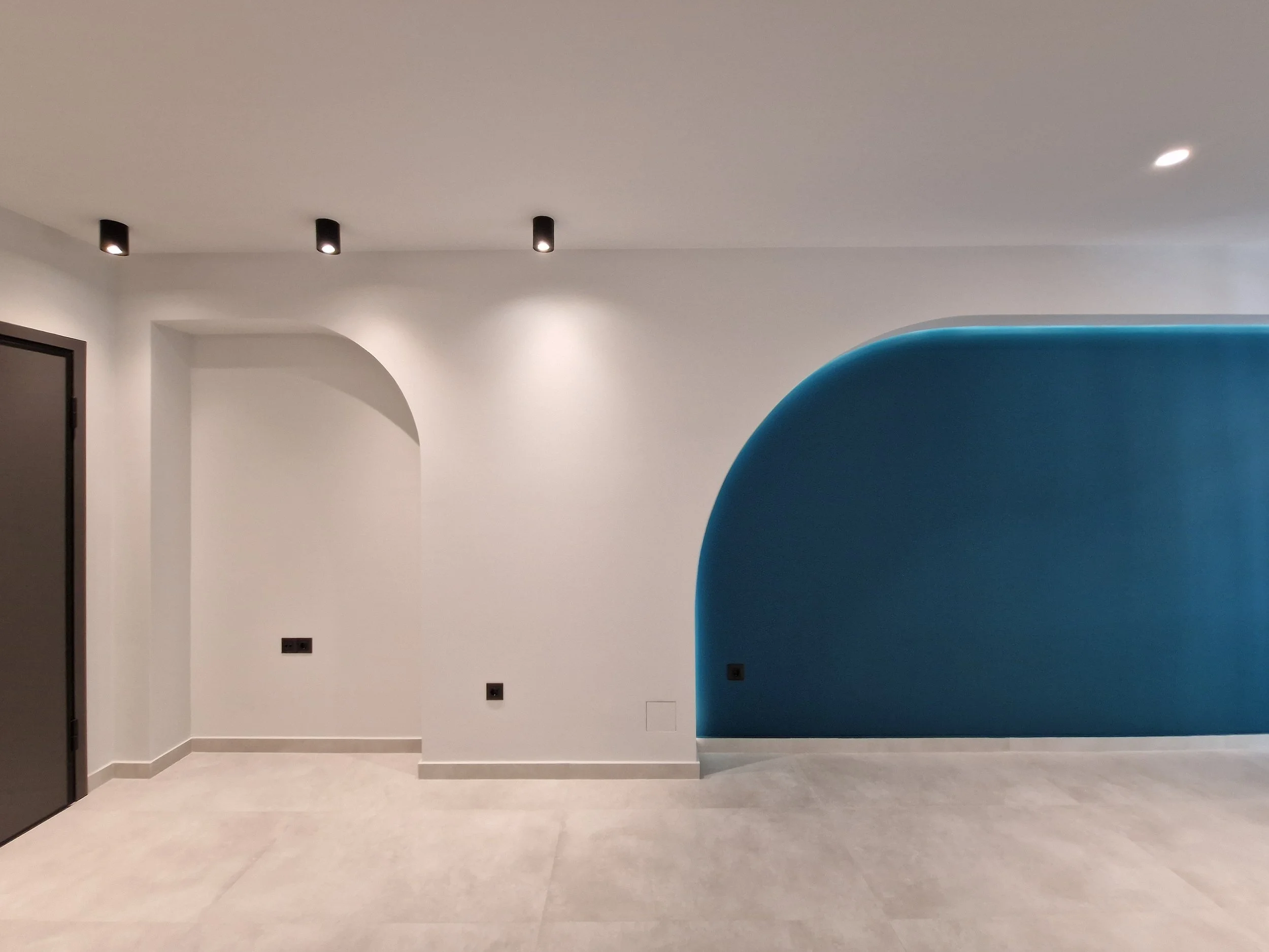 Interior room with white walls, a blue curved partition, and multiple ceiling spotlights.