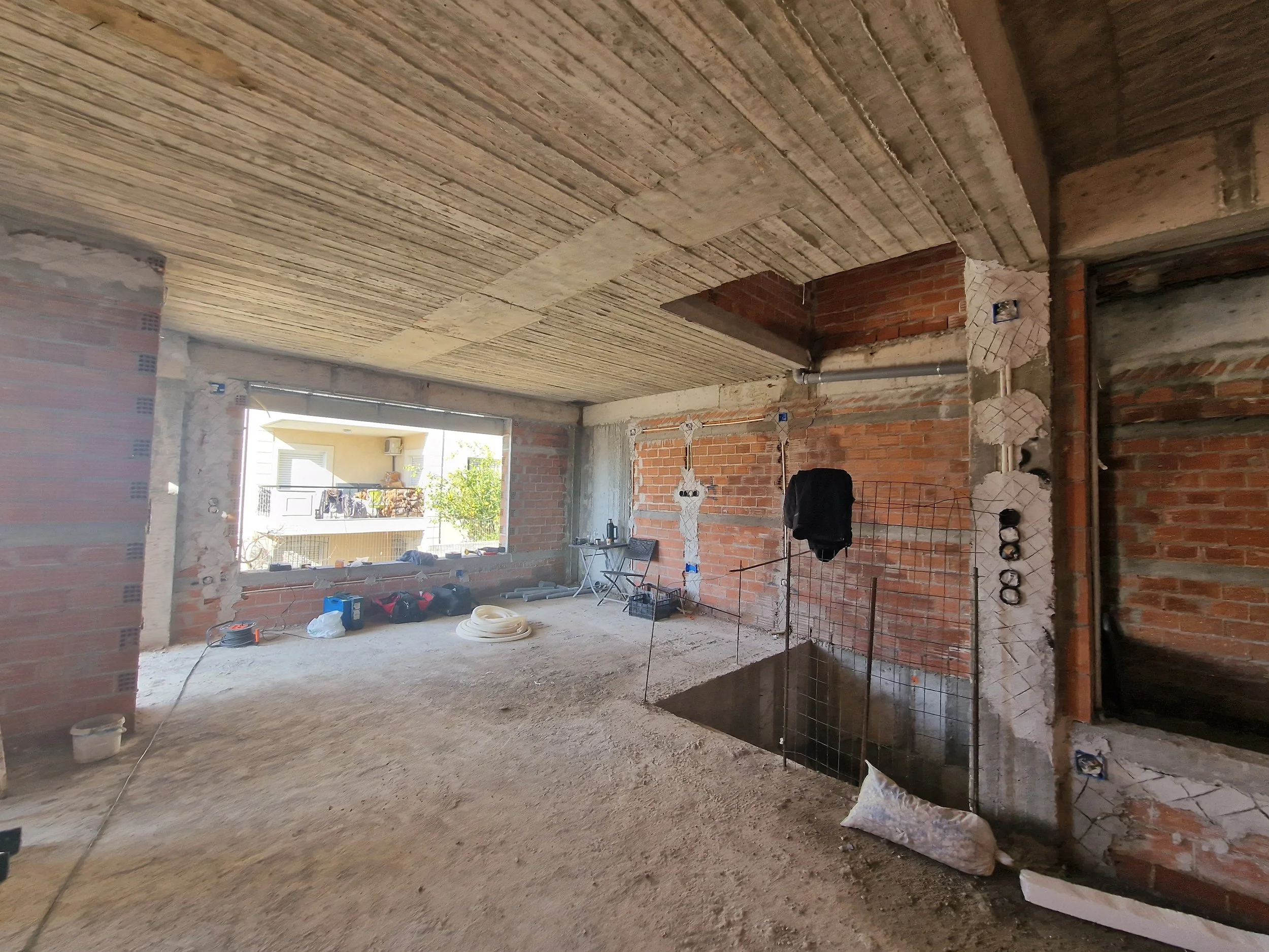 Interior of a building under construction with exposed brick walls, a concrete ceiling, and construction materials and tools scattered on the unfinished floor.