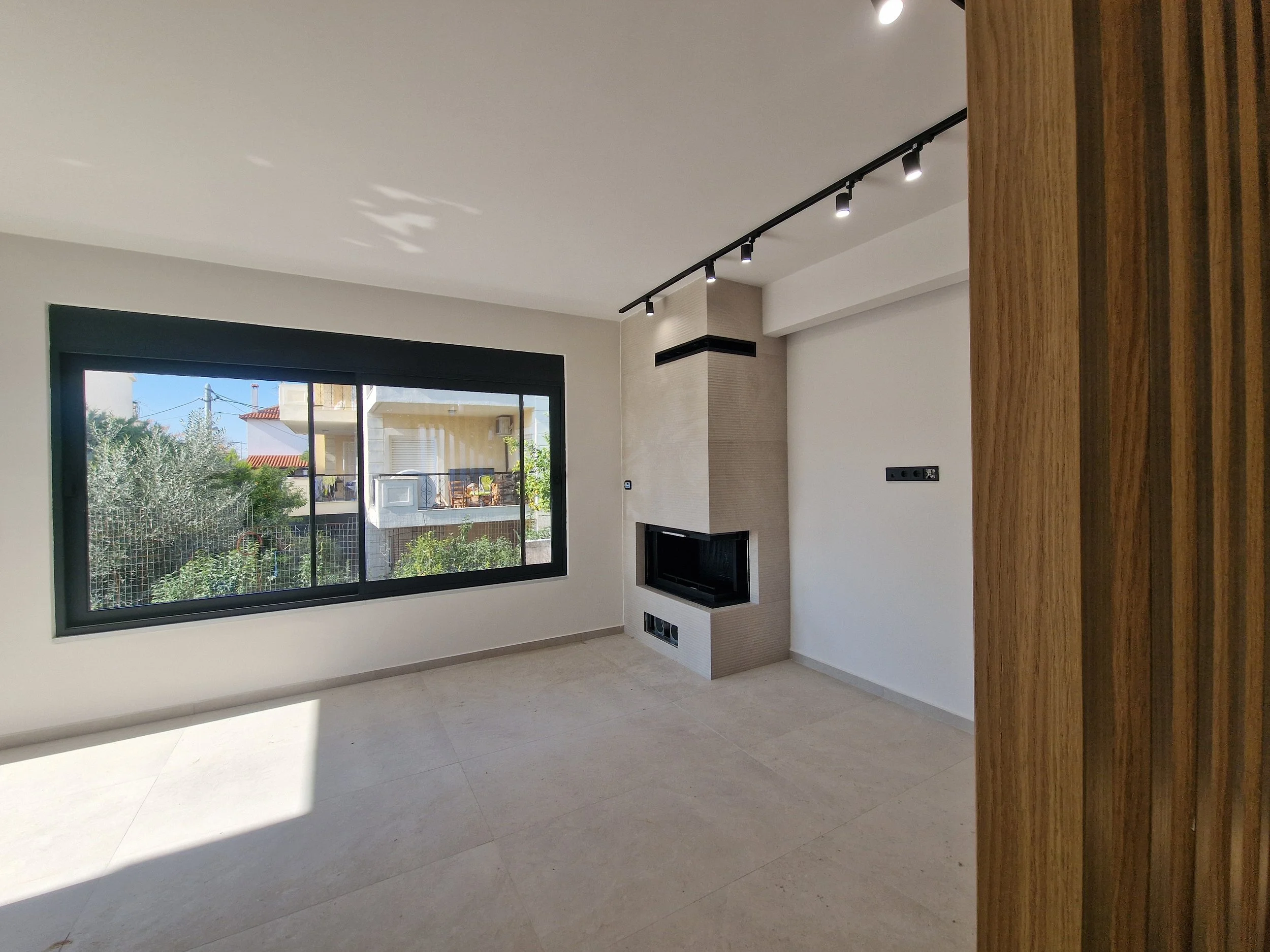 Interior room with large window, view of neighboring buildings, fireplace, and wood panelled partition.