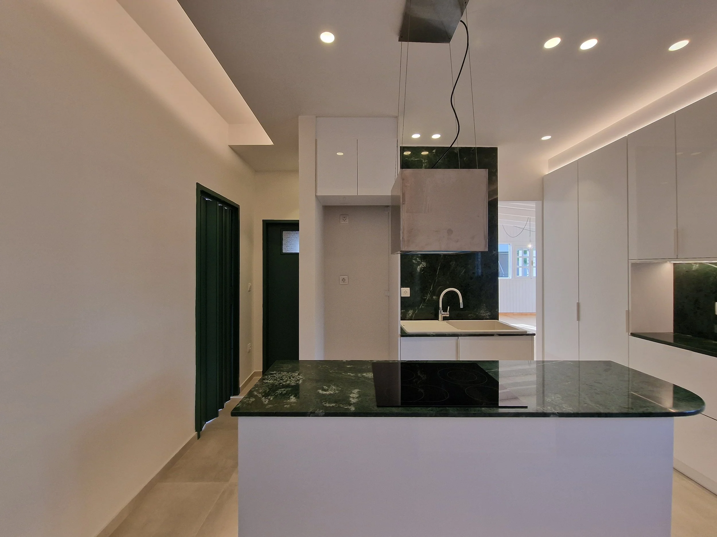 Modern kitchen with white cabinets, black marble countertops, a marble range hood, and green walls.