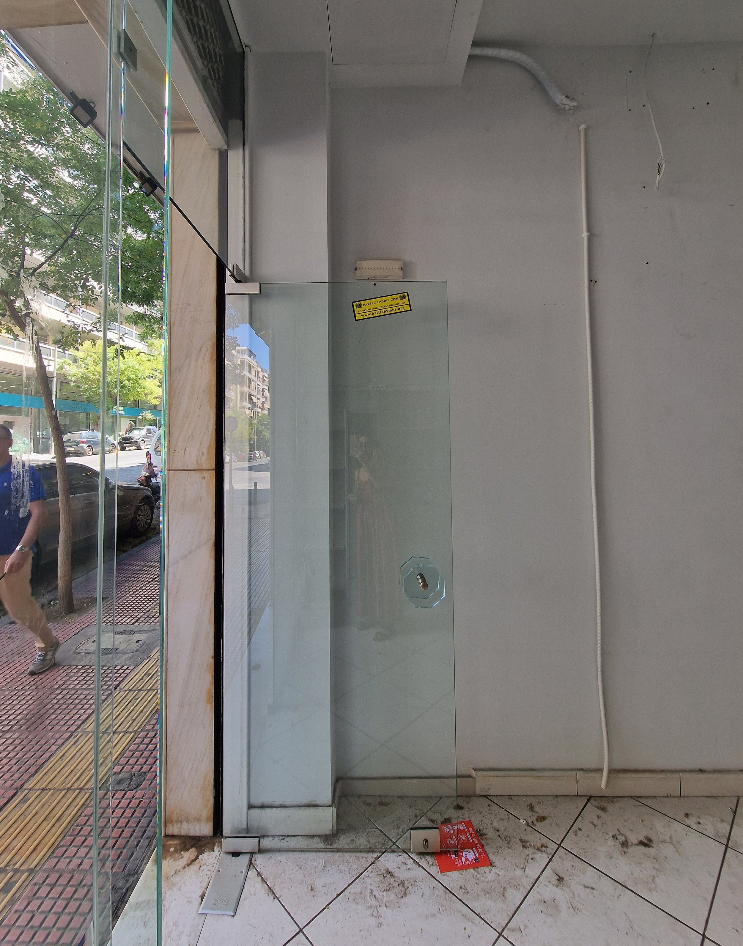 Interior of a cleaning or maintenance area with a glass door, electrical conduit, and scattered debris on the tiled floor inside and outside the doorway.