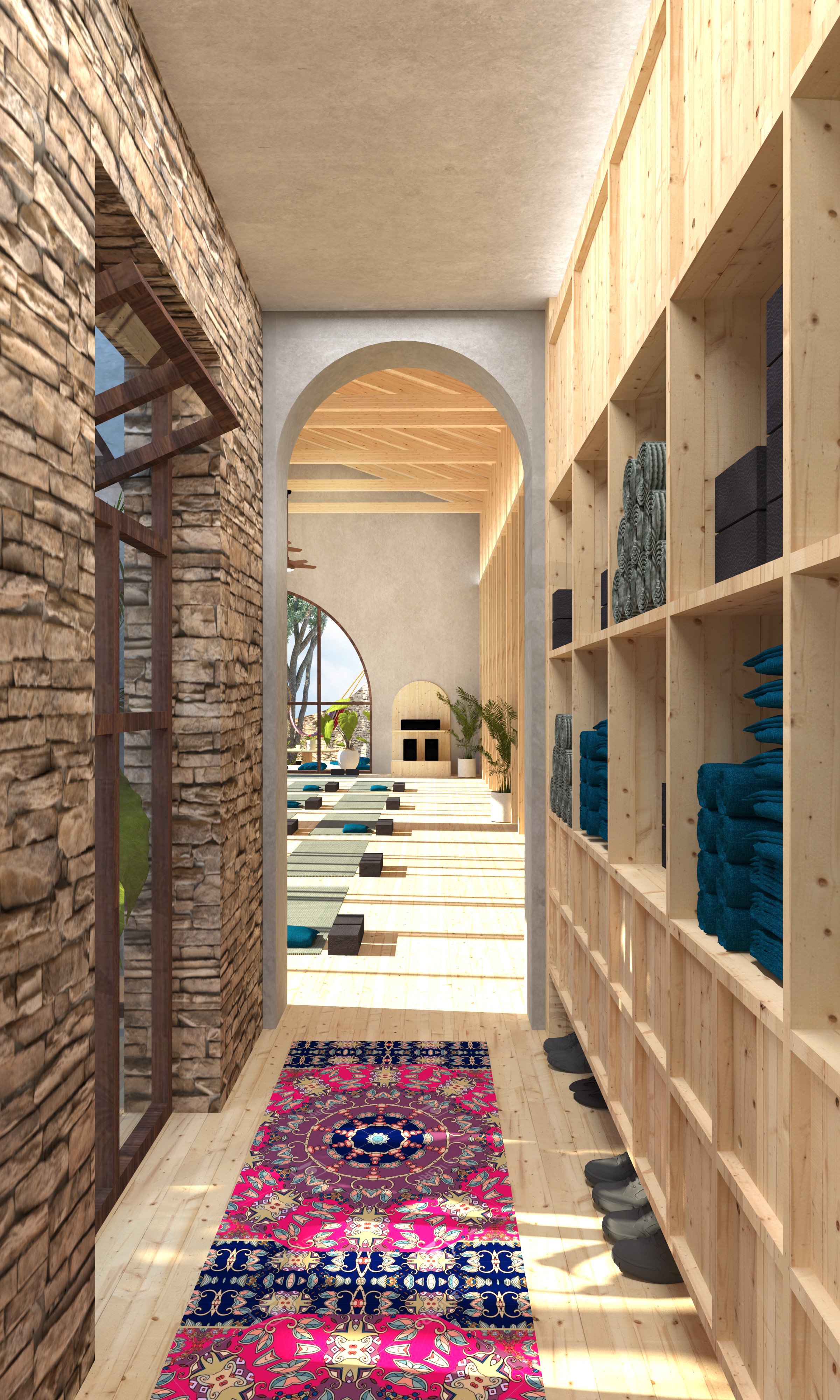 Interior view of a cozy room with wooden shelves on the right stocked with rolled towels and shoes, a colorful oriental rug on the floor, a stone wall on the left with a window, and a view of a sunny outdoor area through an arched doorway and window.