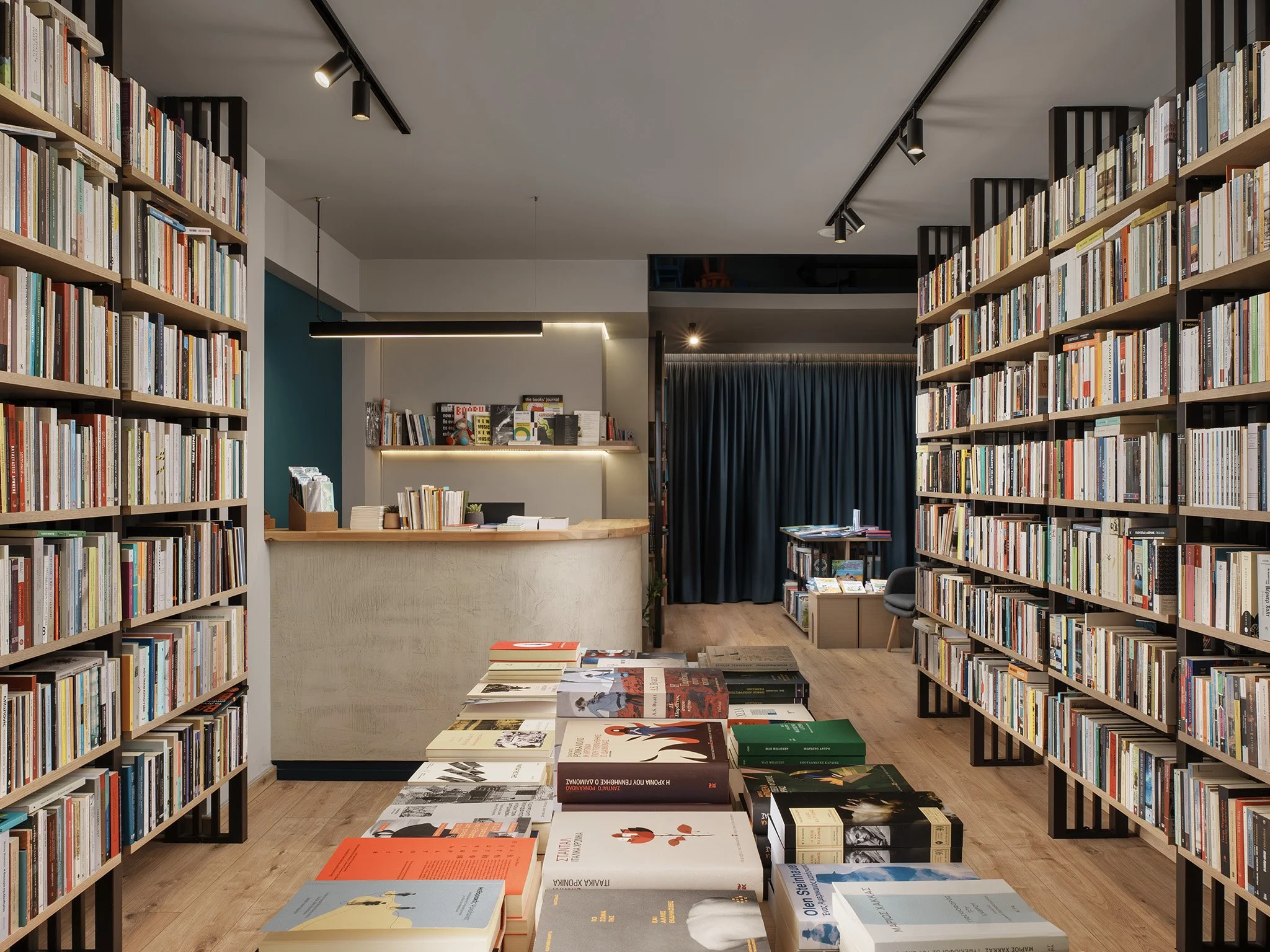 Interior of a bookstore with tall wooden bookshelves filled with books on both sides, a display table with books in the center, and a checkout counter in the background.