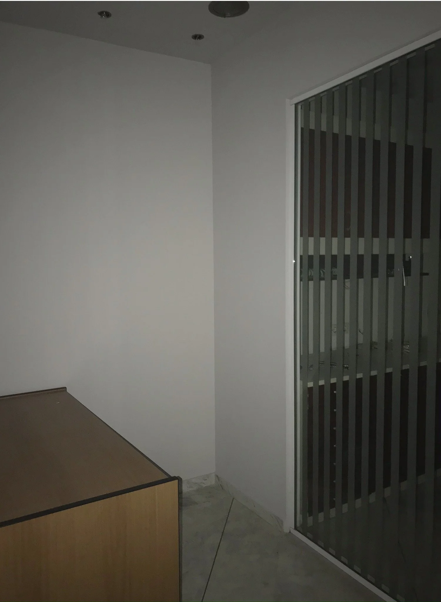 Empty room with white walls, a corner window with vertical blinds, a wooden table or cabinet, and tiled floor.