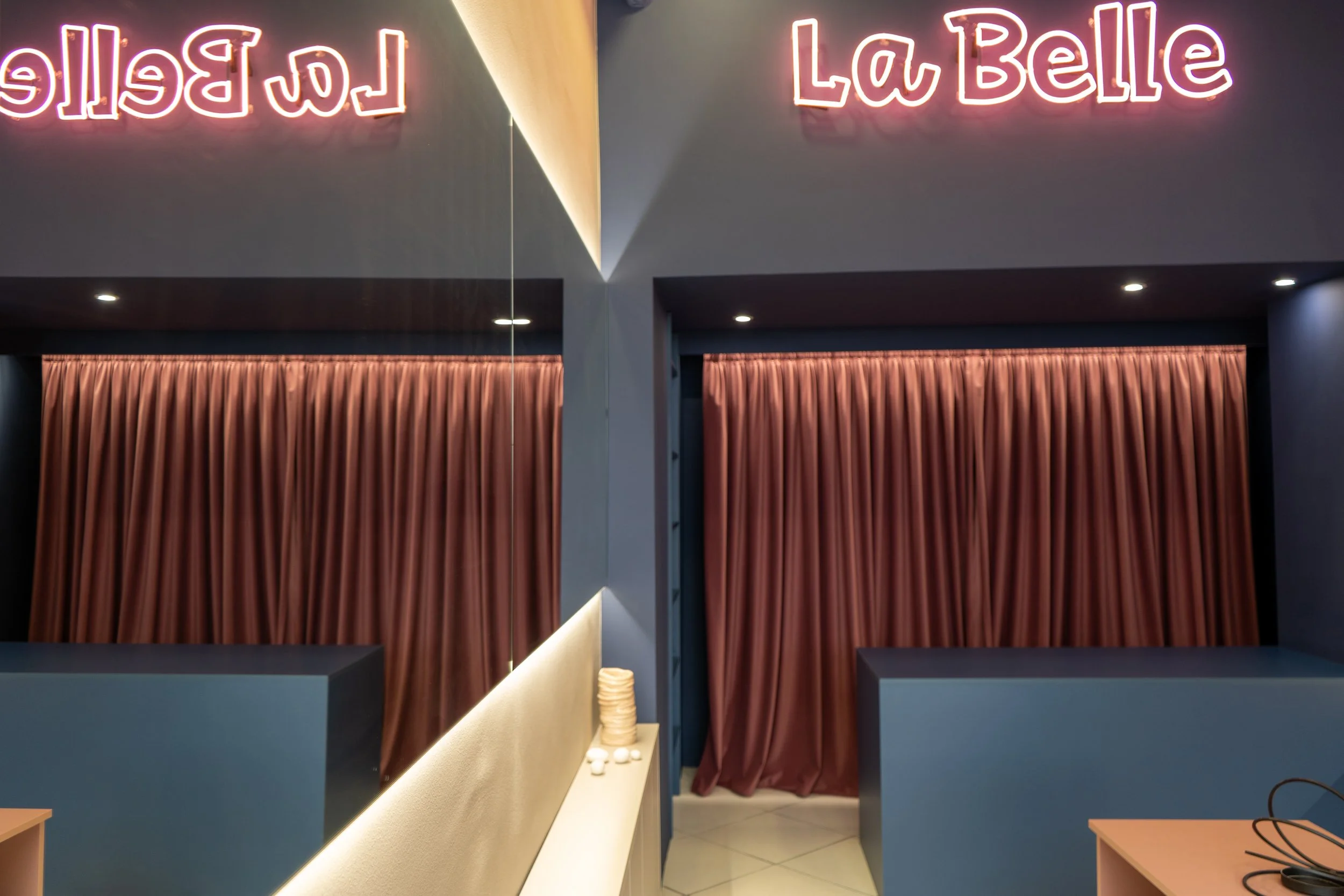 Interior of a restaurant with pink neon sign reading 'La Belle' and pink curtains.