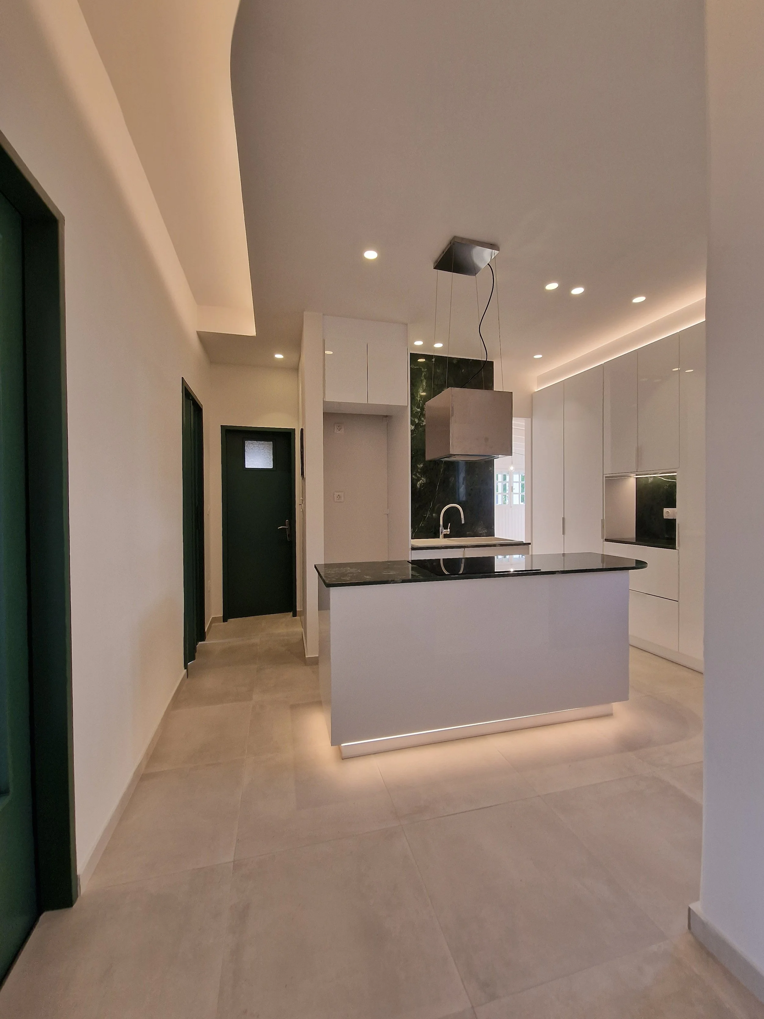 Modern kitchen with white cabinets, black marble backsplash, and a stainless steel range hood. The room has recessed lighting and light-colored tiled flooring.