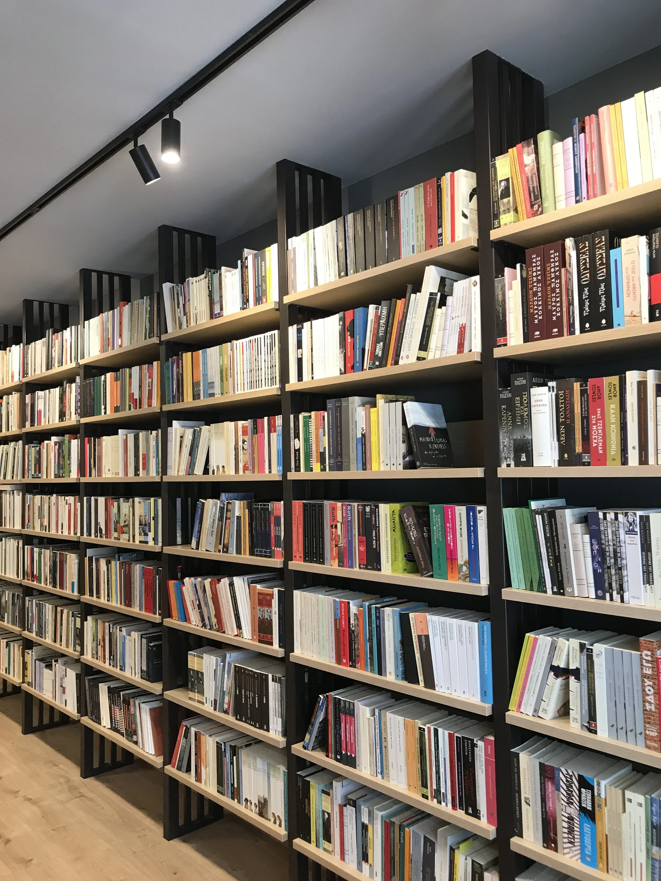 Stereoscopic bookshelves filled with various books in a library or bookstore, with overhead lighting and wooden flooring.