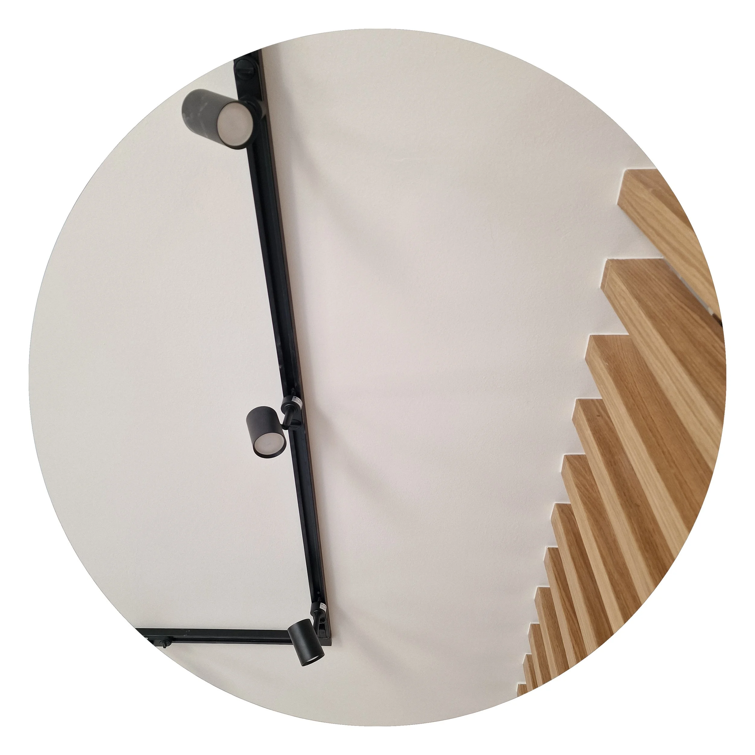 Close-up of a modern black track light fixture mounted on a white ceiling near wooden stairs.