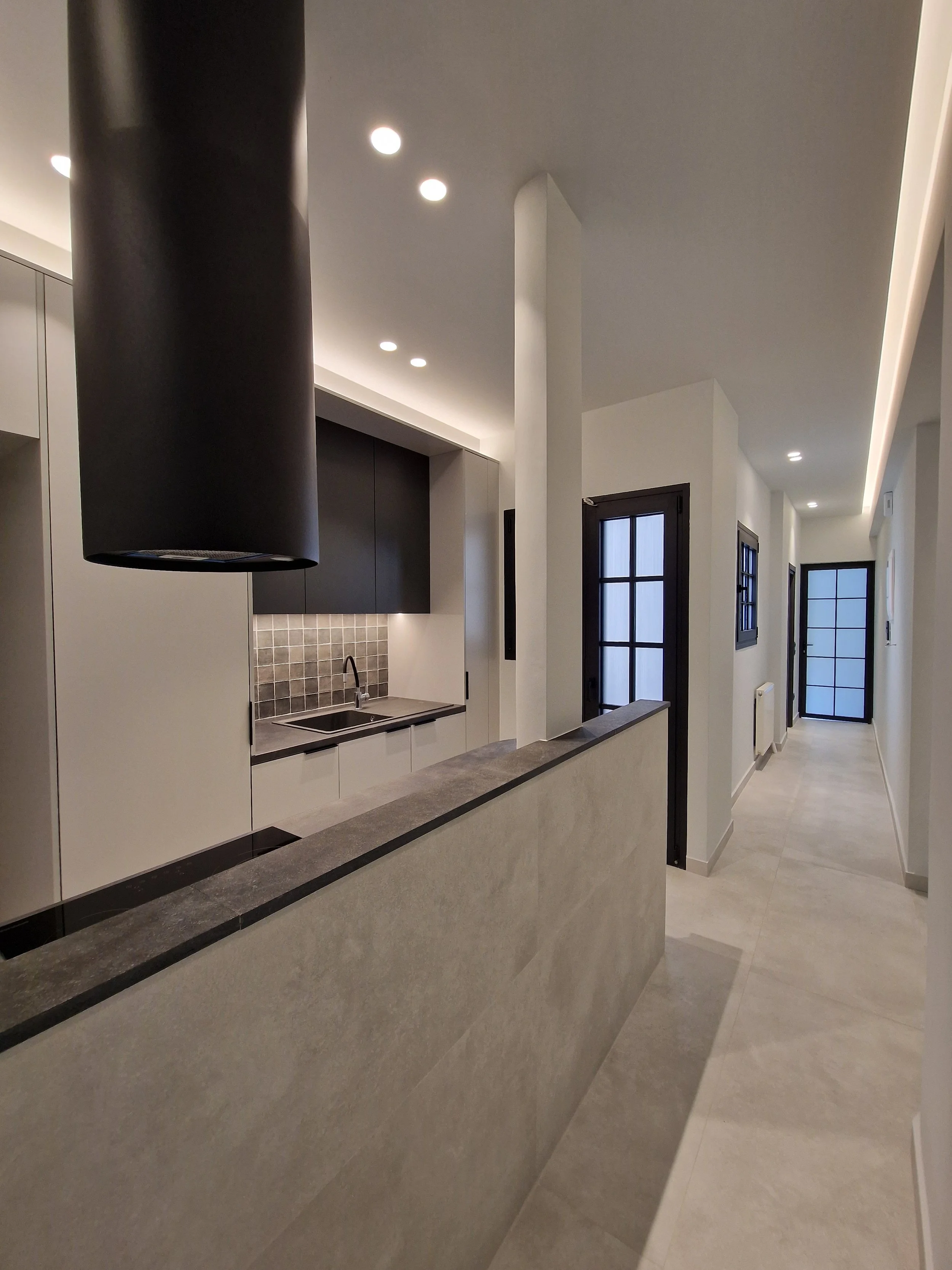 Modern interior hallway with white walls, black-framed glass doors, and recessed lighting ceiling, leading to a door at the end.