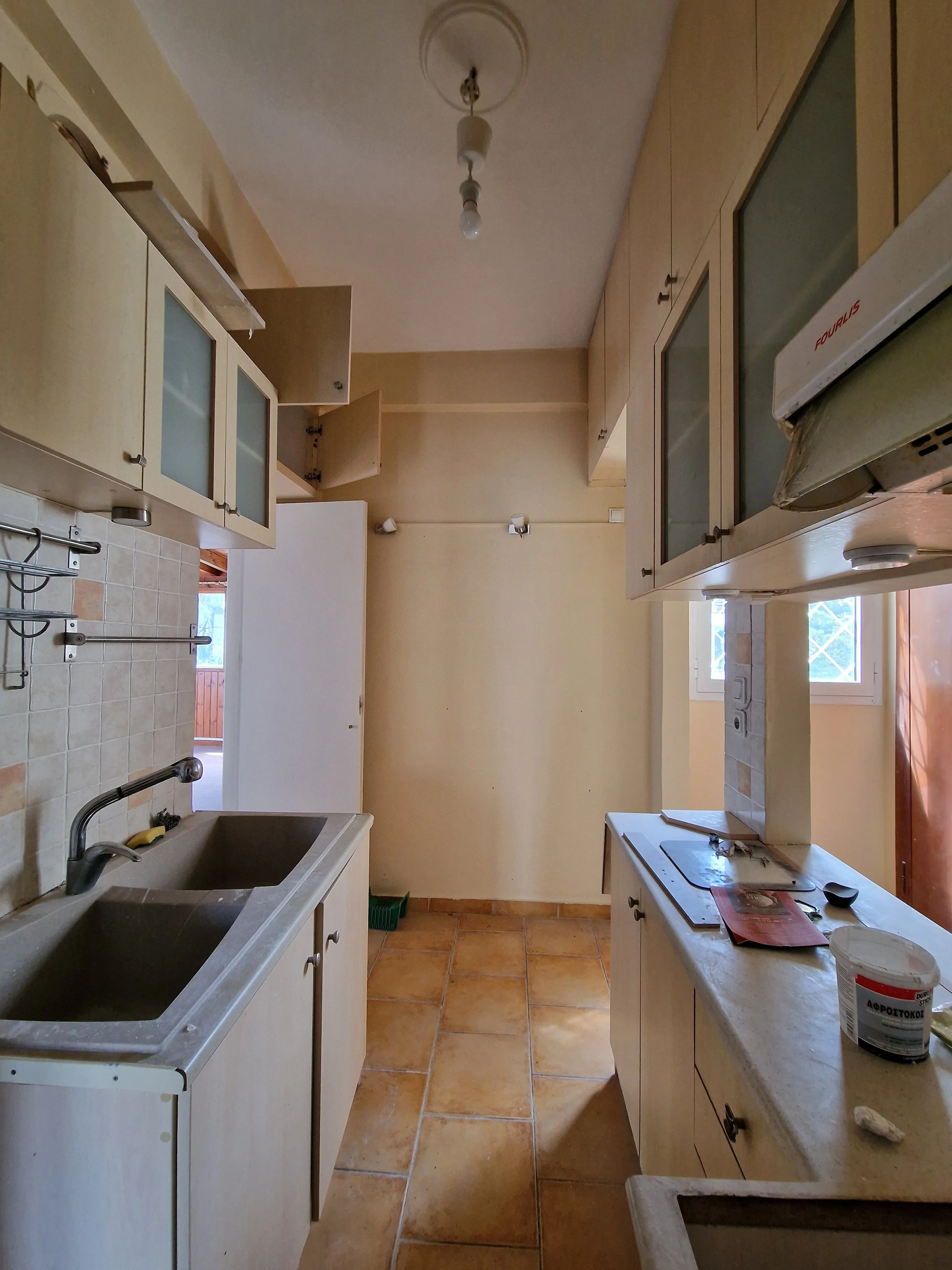 A kitchen under renovation with open cabinets, a sink, a countertop, and various construction items.