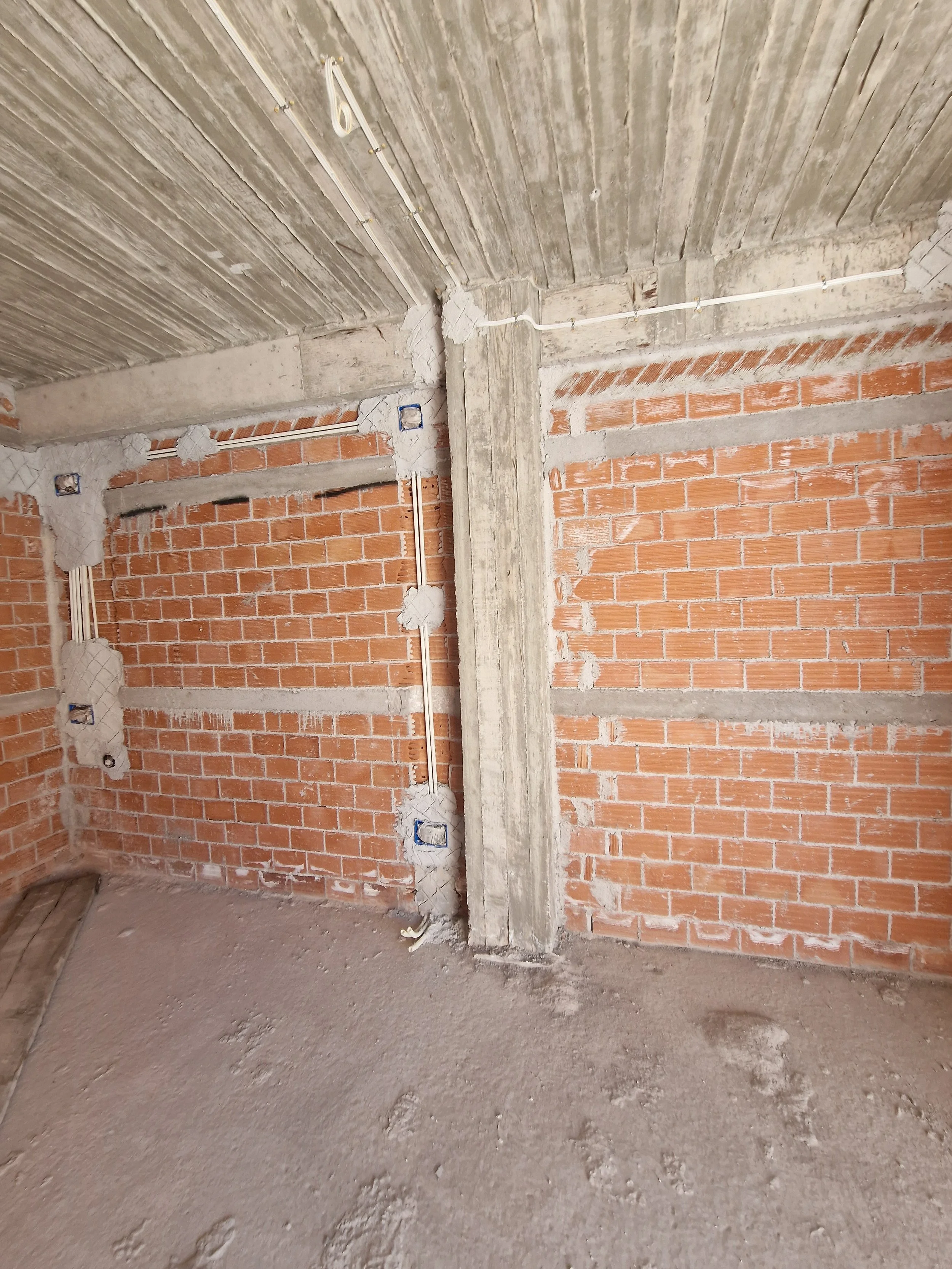 Interior view of an unfinished room under construction, with brick walls, exposed electrical wiring, concrete column, and a bare concrete floor.