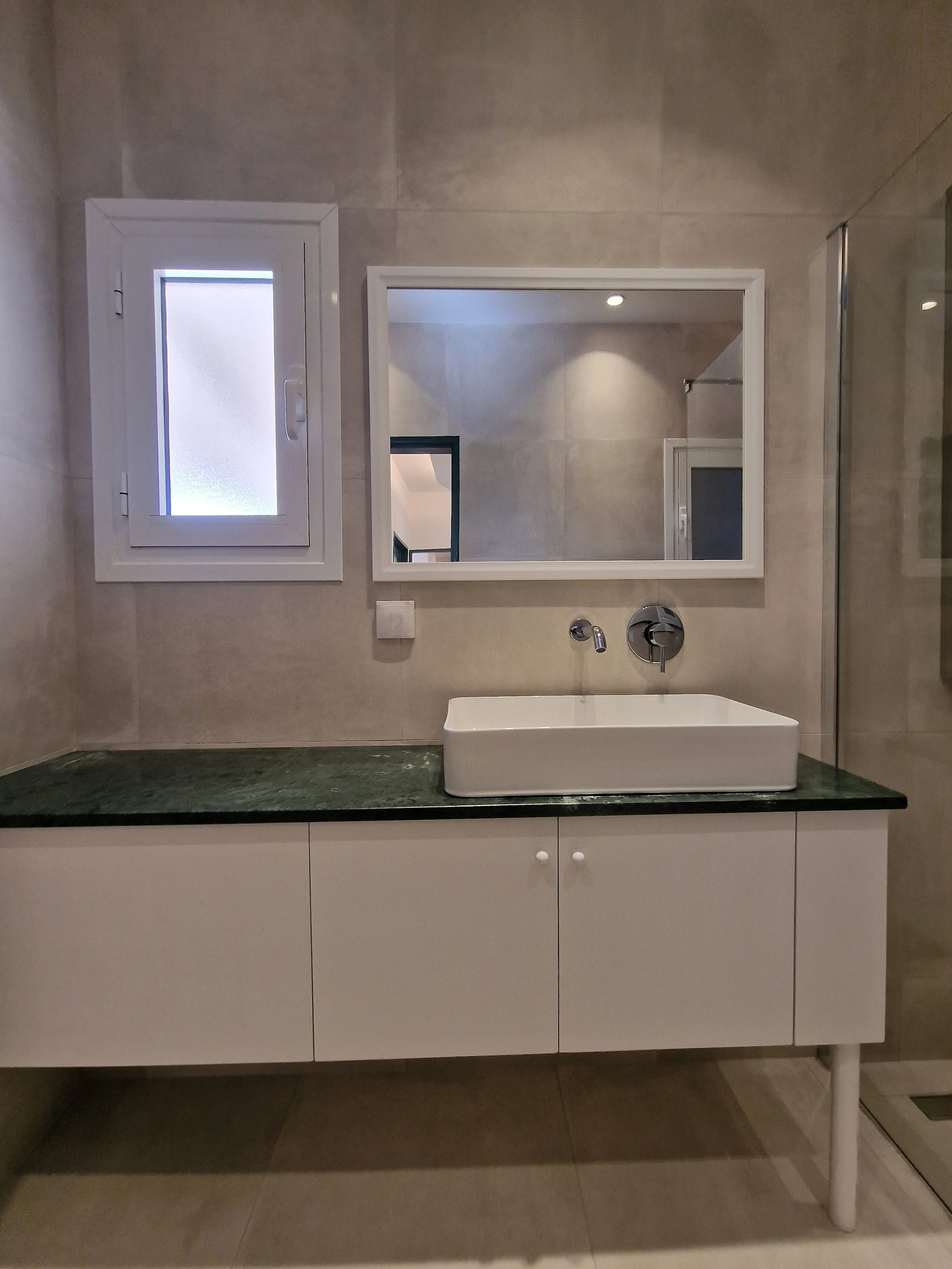 Modern bathroom with a white sink, a mirror, a frosted window, and beige tiled walls and floor.