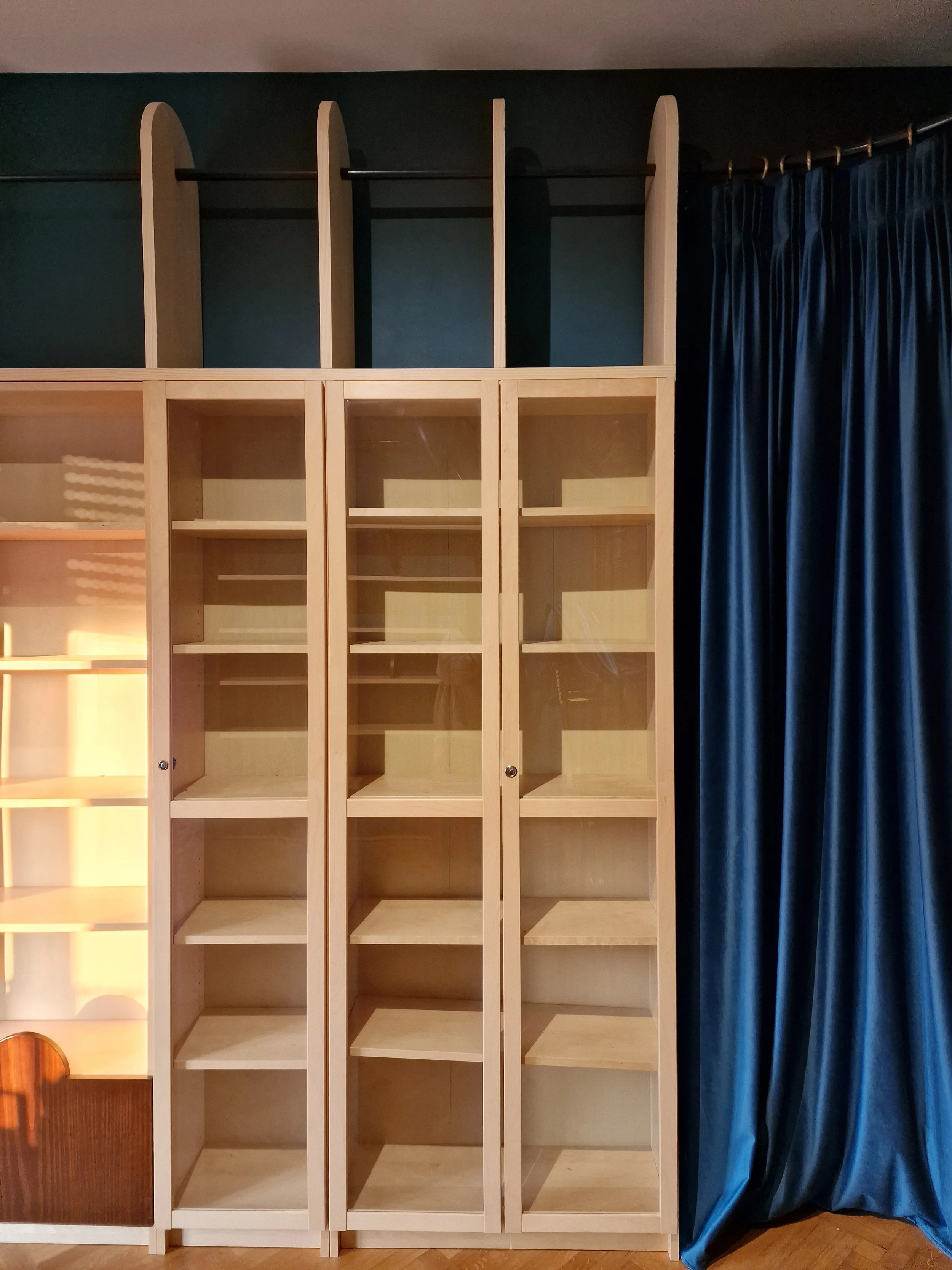 Empty wooden shelving unit with glass doors next to dark blue curtains in a room.