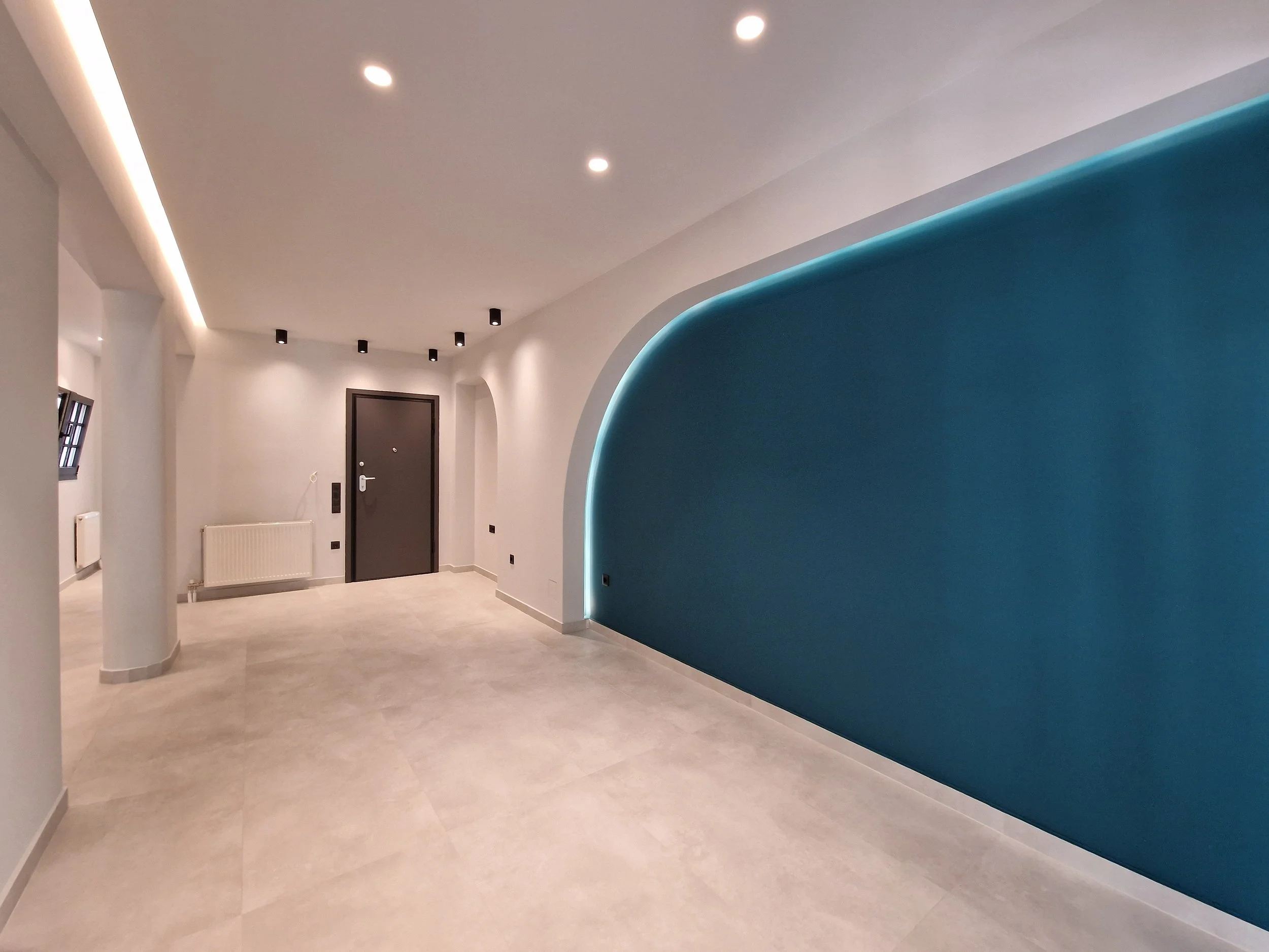Modern interior hallway with curved blue accent wall, ceiling lights, and a black front door.