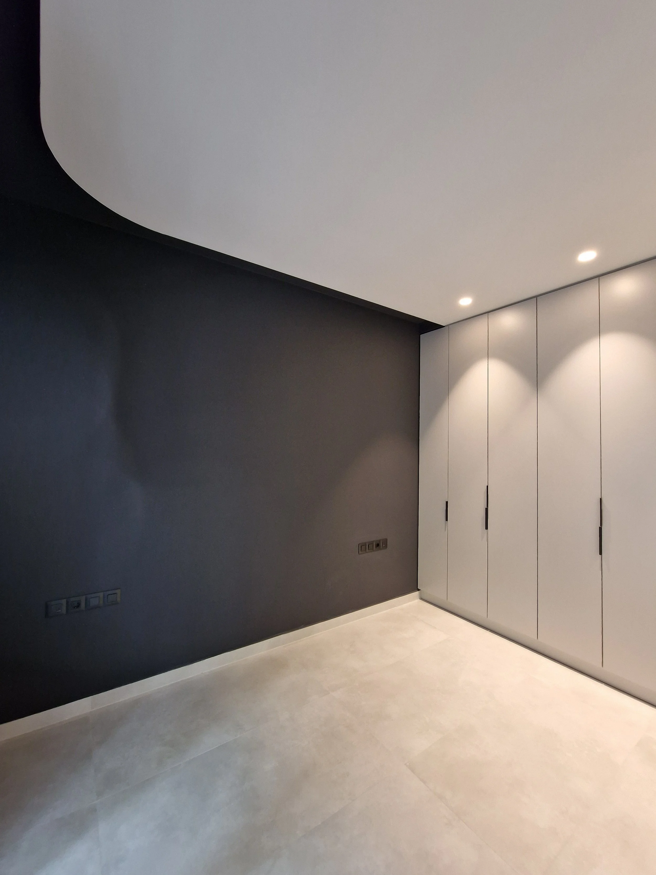 A modern room with a dark gray wall, white ceiling, and a row of white closets.