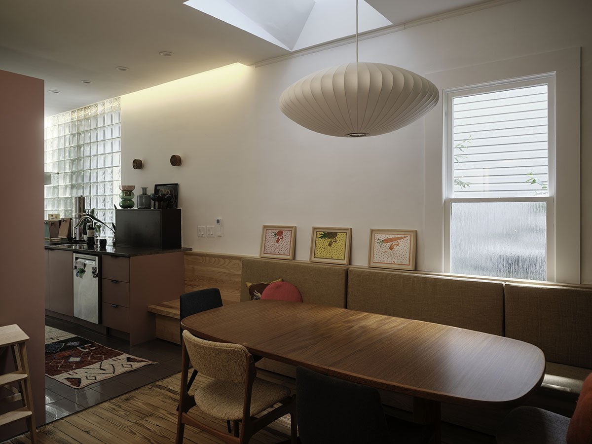 Living room with a dining table, patterned artwork, window, and a kitchen area visible in the background.