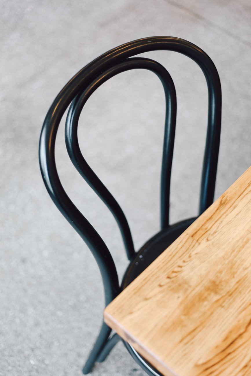 A black metal chair with curved backrest next to a wooden table on a gray floor.