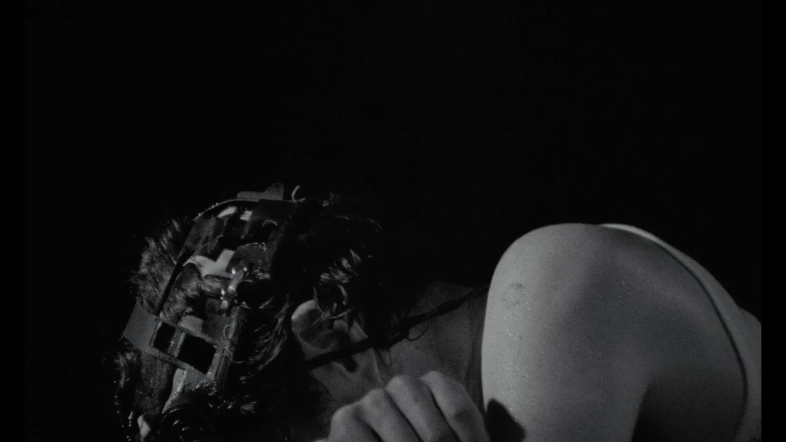 A person in a dark setting wears a helmet and headphones, with their hand on a white megaphone or loudspeaker.