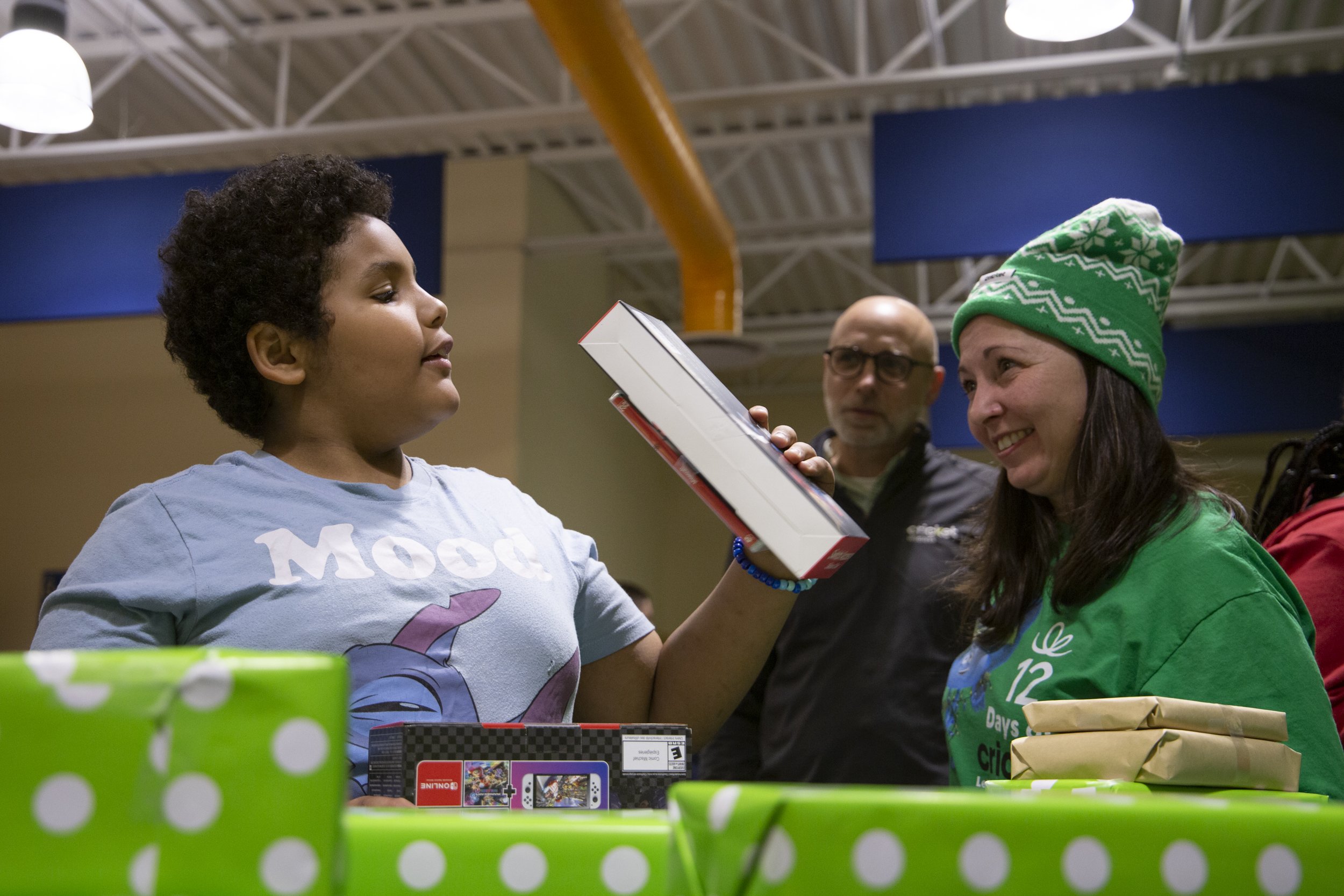 A child from the Reed-White family opens a gift as Cricket Wireless marketing manager Heather Omahne looks on during a surprise holiday giveaway on Dec. 4, 2024. The Reed-White, Isaac and Nelson families — all longtime members of Rochester’s Boys & G