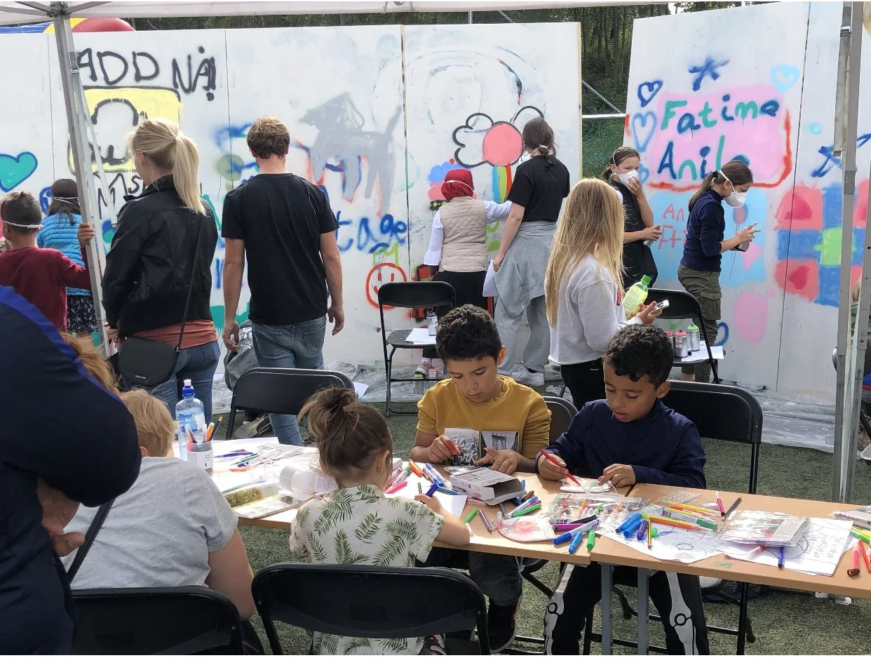 Barn og voksne som maler graffiti på en vegg under en utendørs aktivitet.