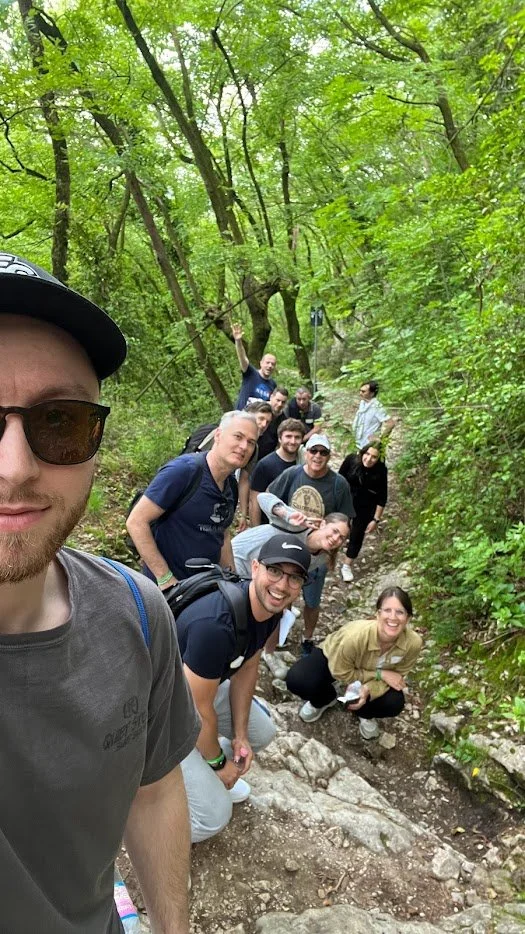 Group of people hiking on a forest trail with lush green trees surrounding them, smiling and posing for a photo.