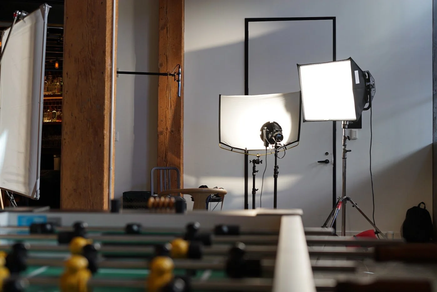 Photography studio with lighting equipment, softbox lights, a gray wall, and a foosball table in the foreground.