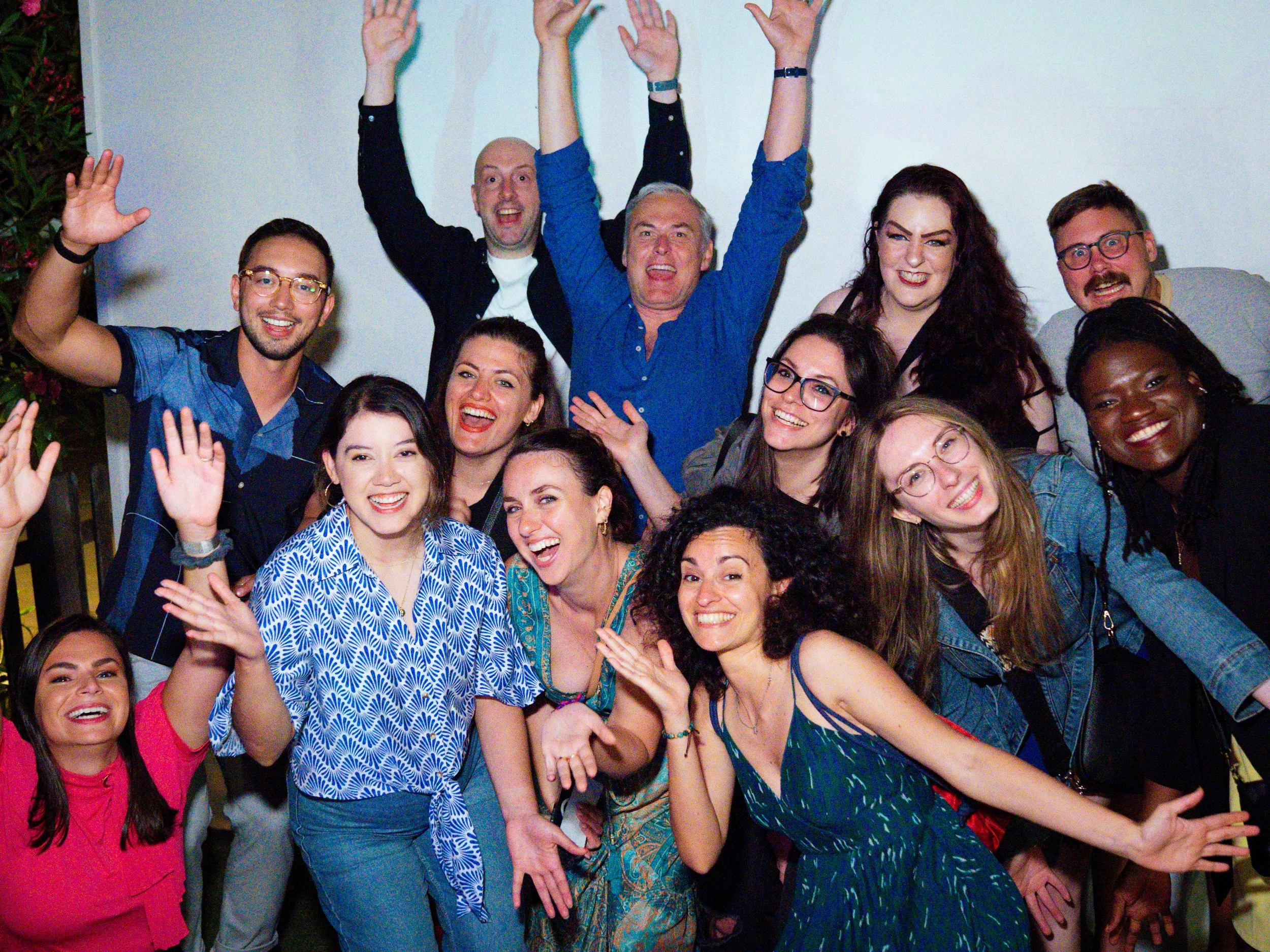 Group of people smiling and waving, celebrating at a gathering or party.