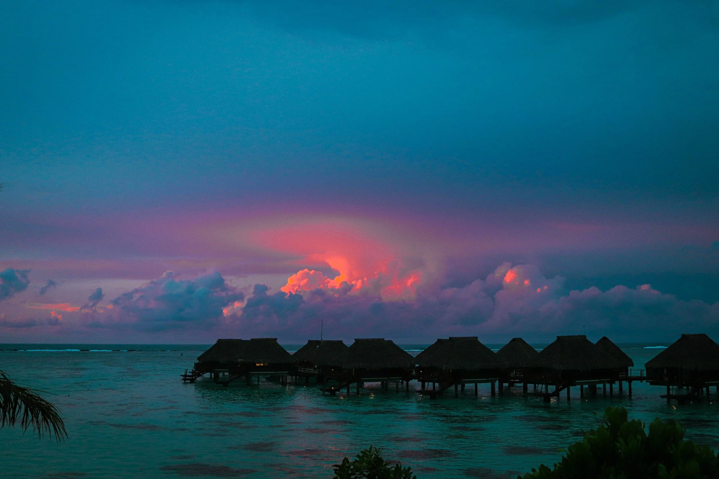 Overwater bungalows at sunset on the ocean with colorful sky and clouds