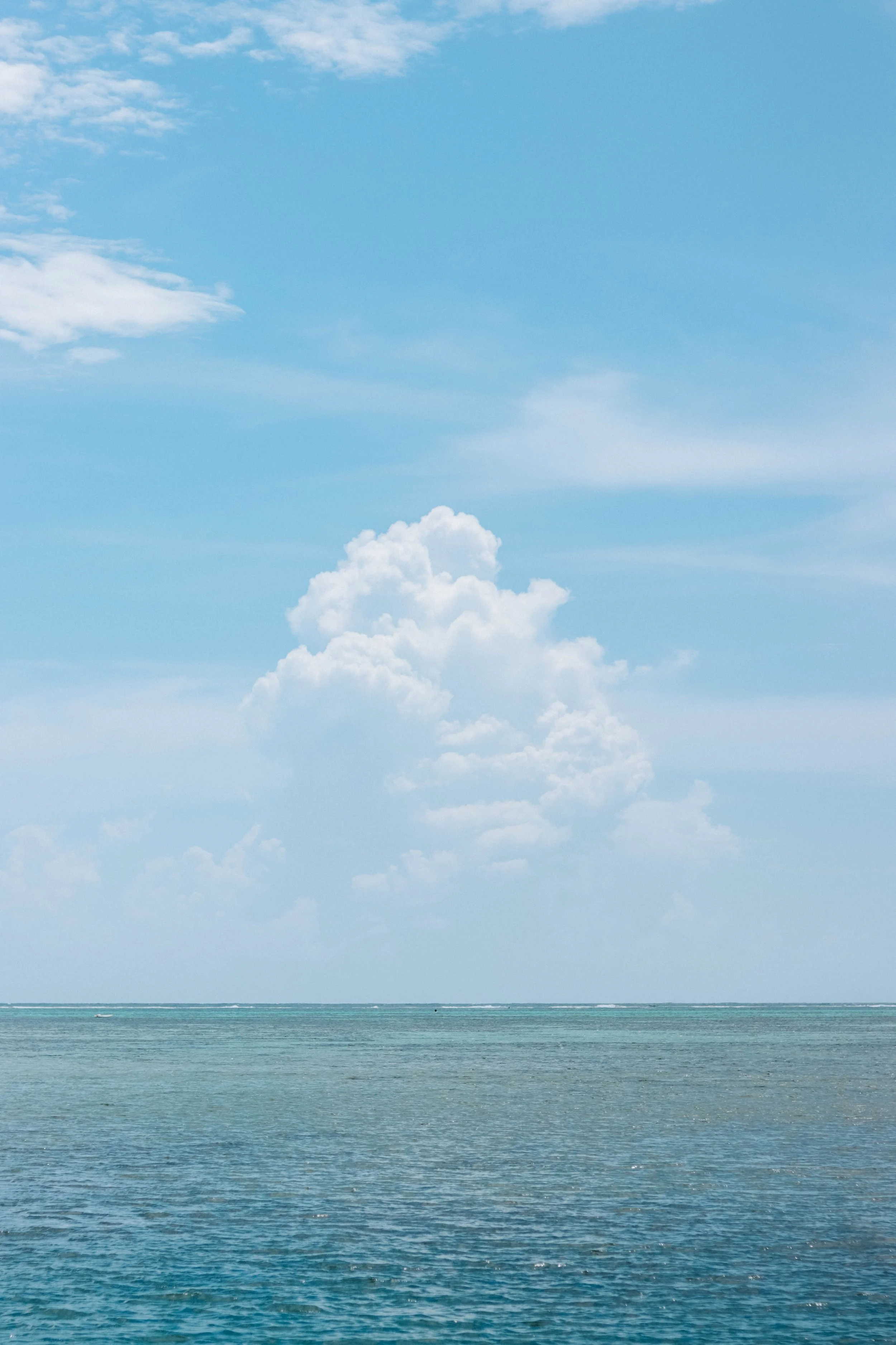 Calm ocean water under a bright blue sky with scattered white clouds.