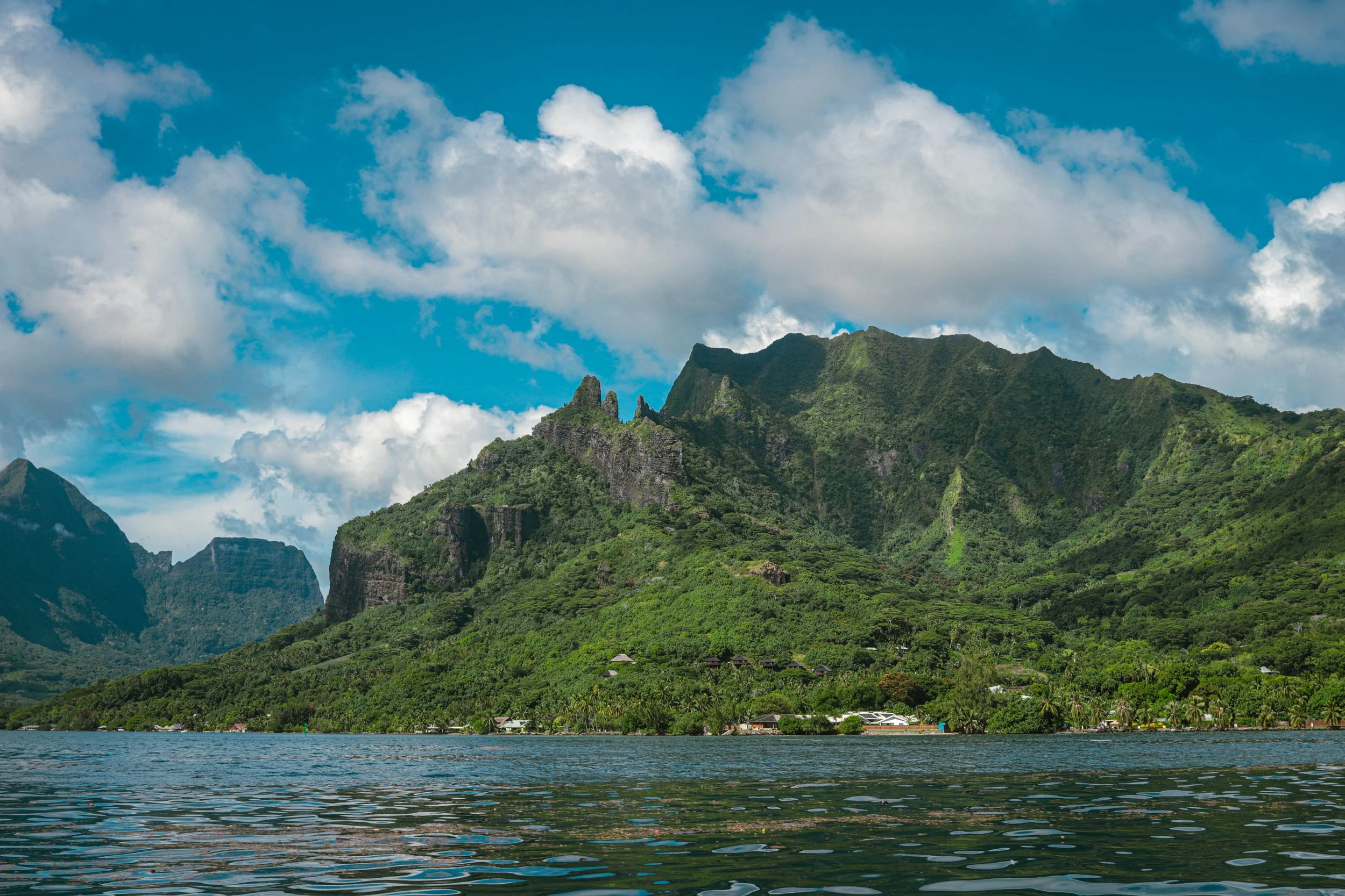Lush green mountain landscape with clouds in the blue sky and water in the foreground.
