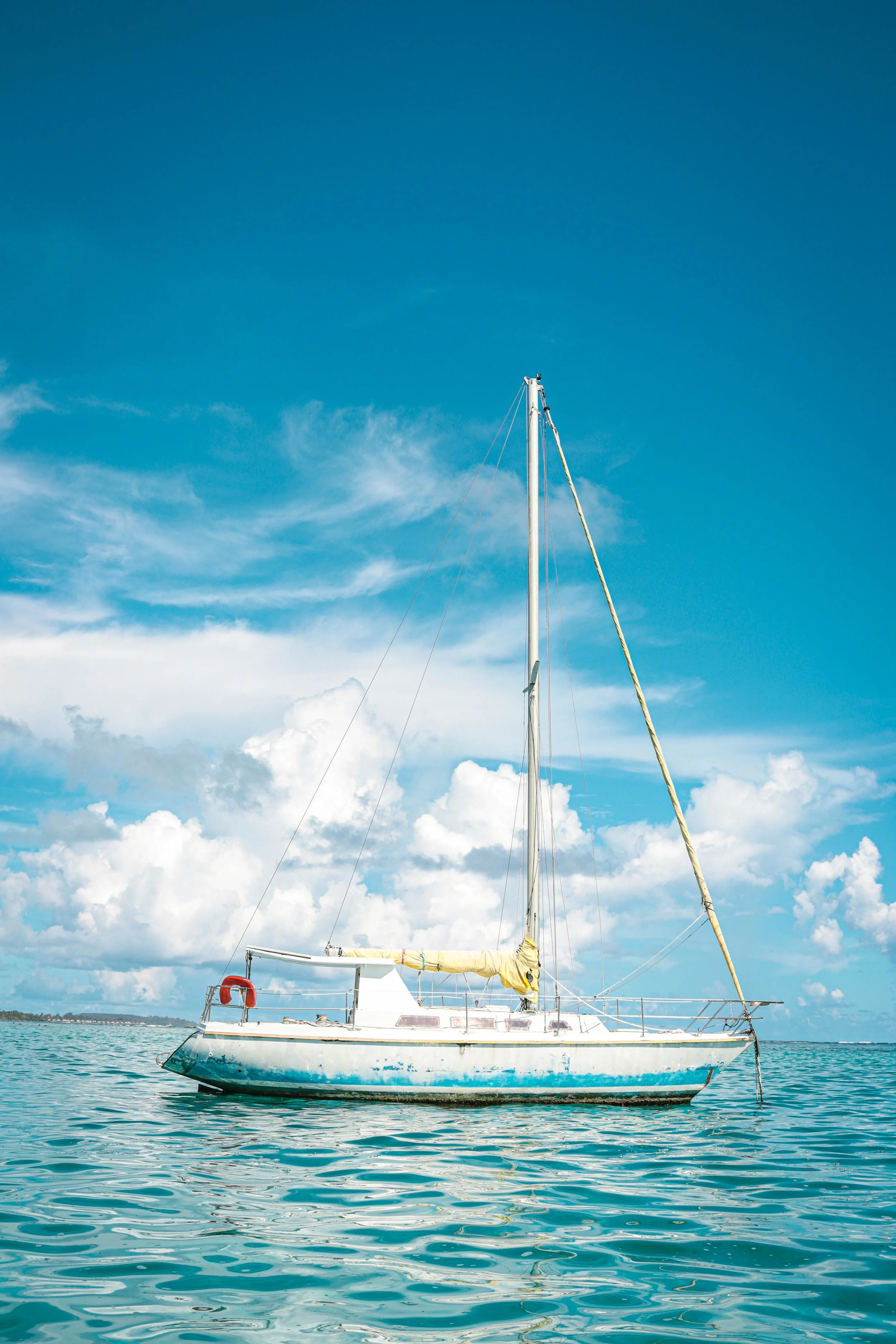 A sailboat floating on calm water under a blue sky with clouds.