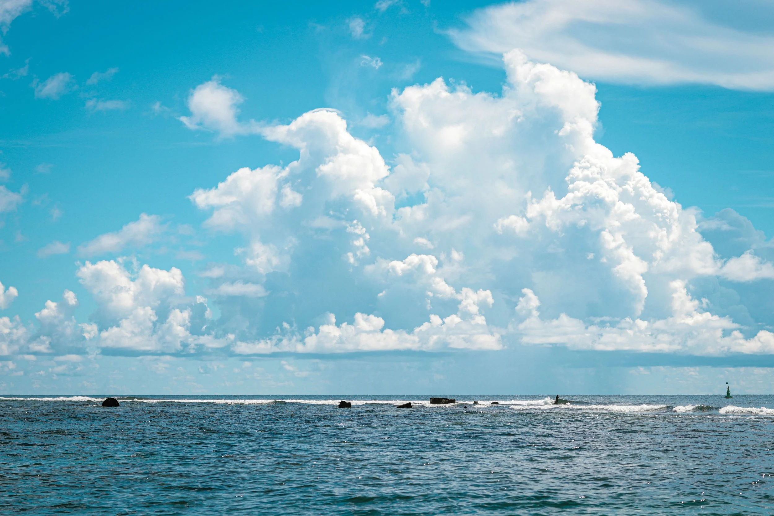 Ocean with gentle waves under a partly cloudy sky featuring large, fluffy white clouds and a distant lighthouse