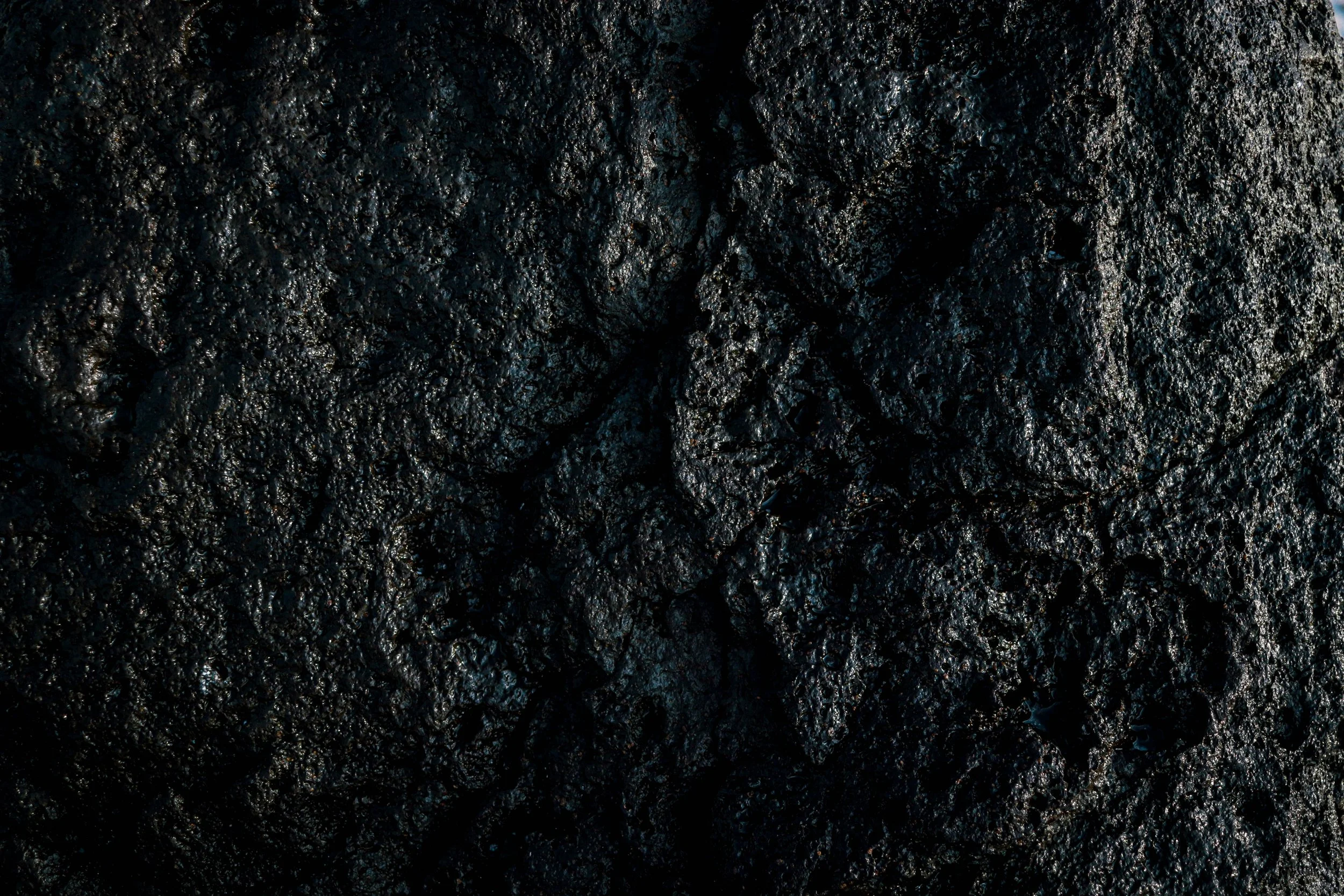 Close-up of black volcanic rock surface with rough, uneven texture and shiny patches.
