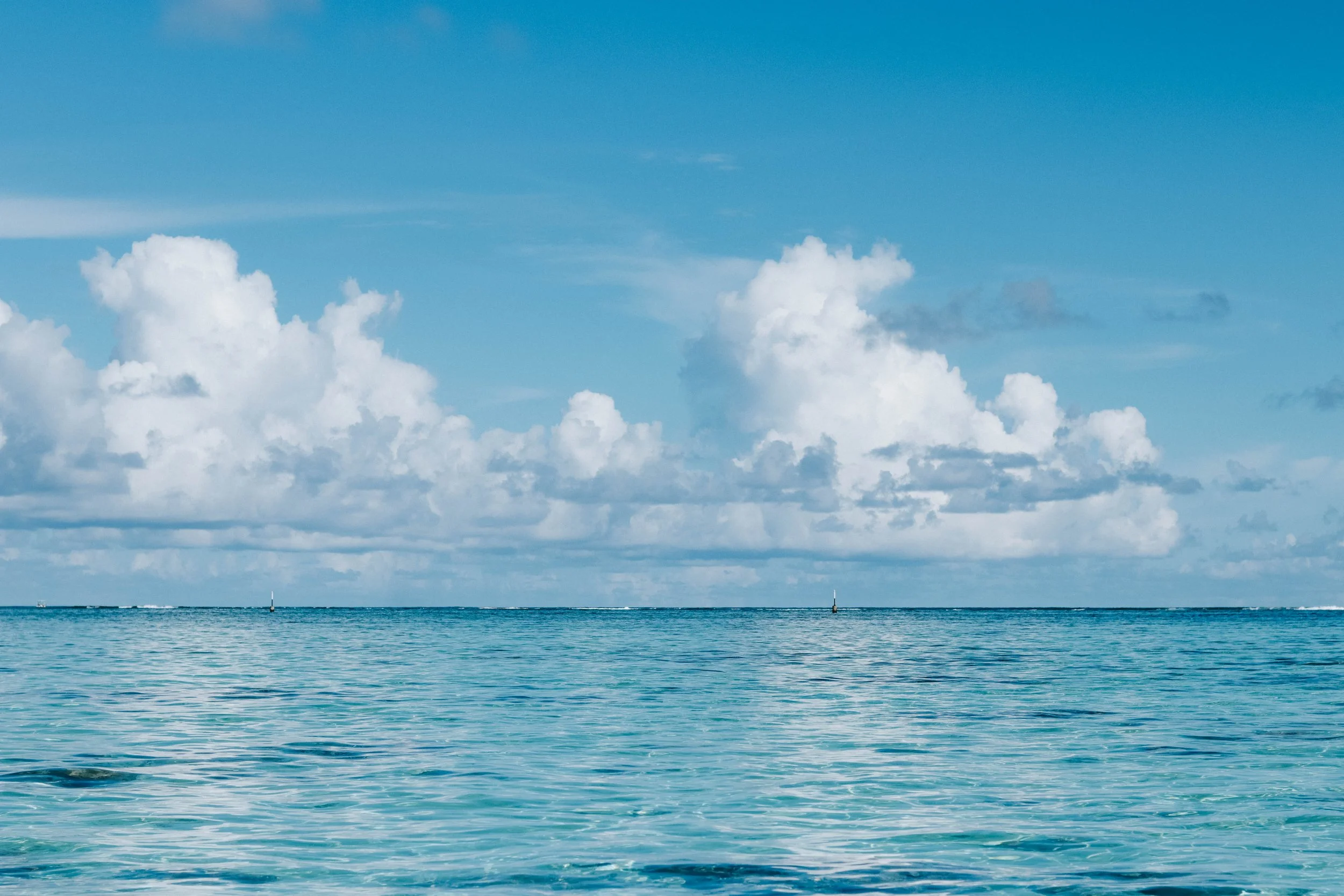 A calm ocean under a blue sky with scattered white clouds.