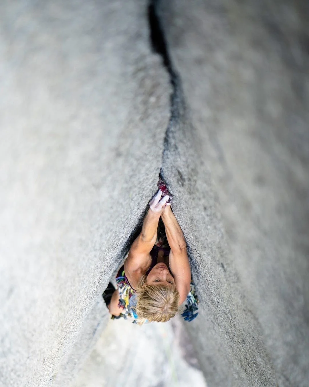 A woman rock climbing on a vertical, textured rock face with her hands gripping a small ledge.