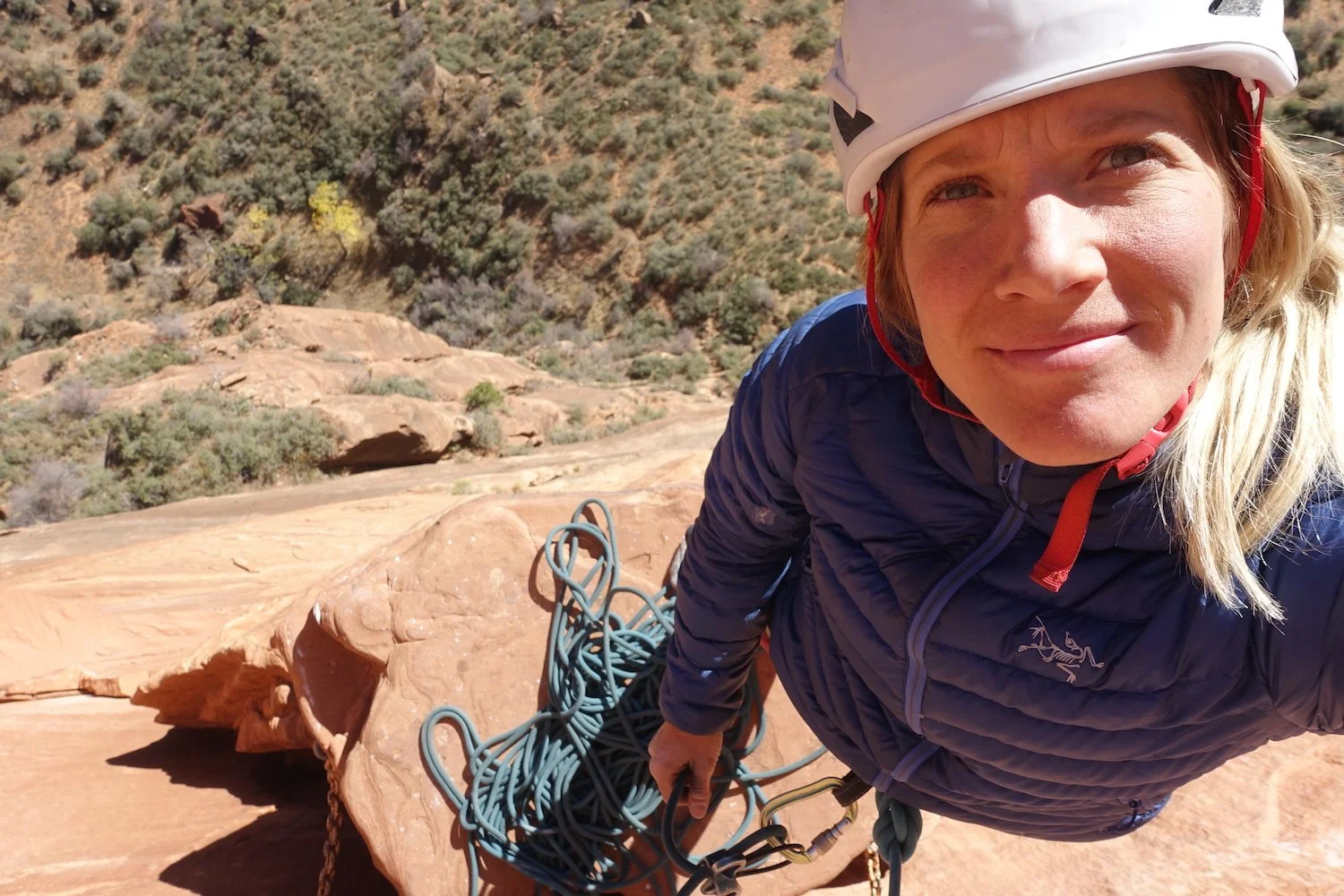 Smiling person in a forest wearing a gray hoodie and cap.