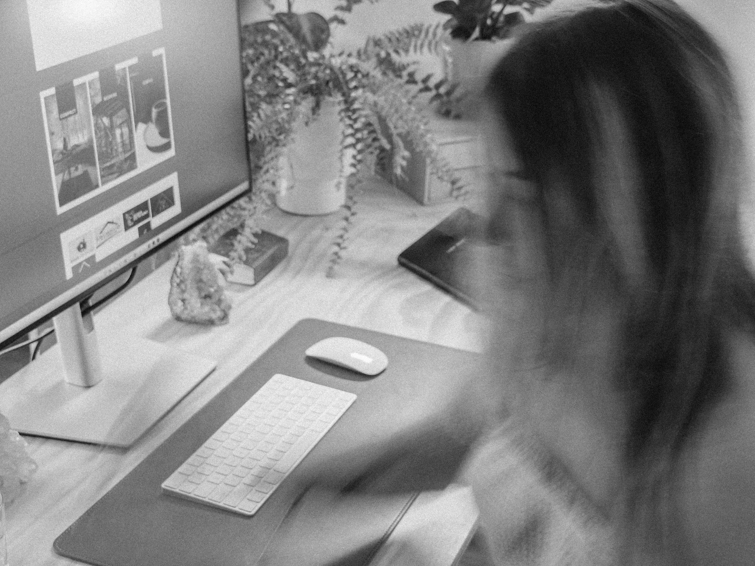 A person working at a desk with a computer monitor, keyboard, and mouse, surrounded by plants and decorative objects.