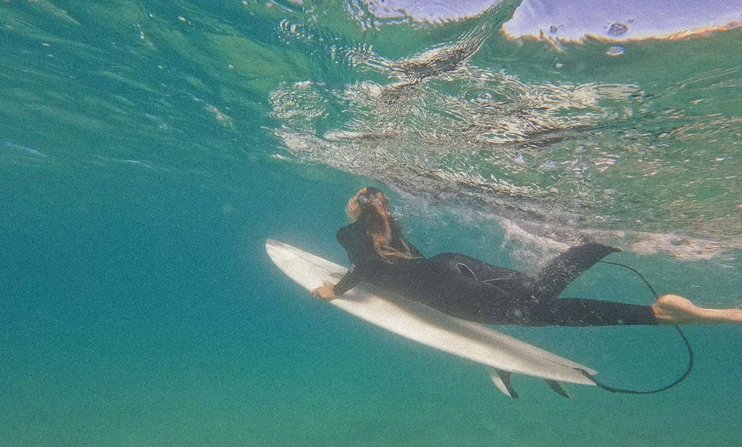A person in a wetsuit riding a surfboard underwater.
