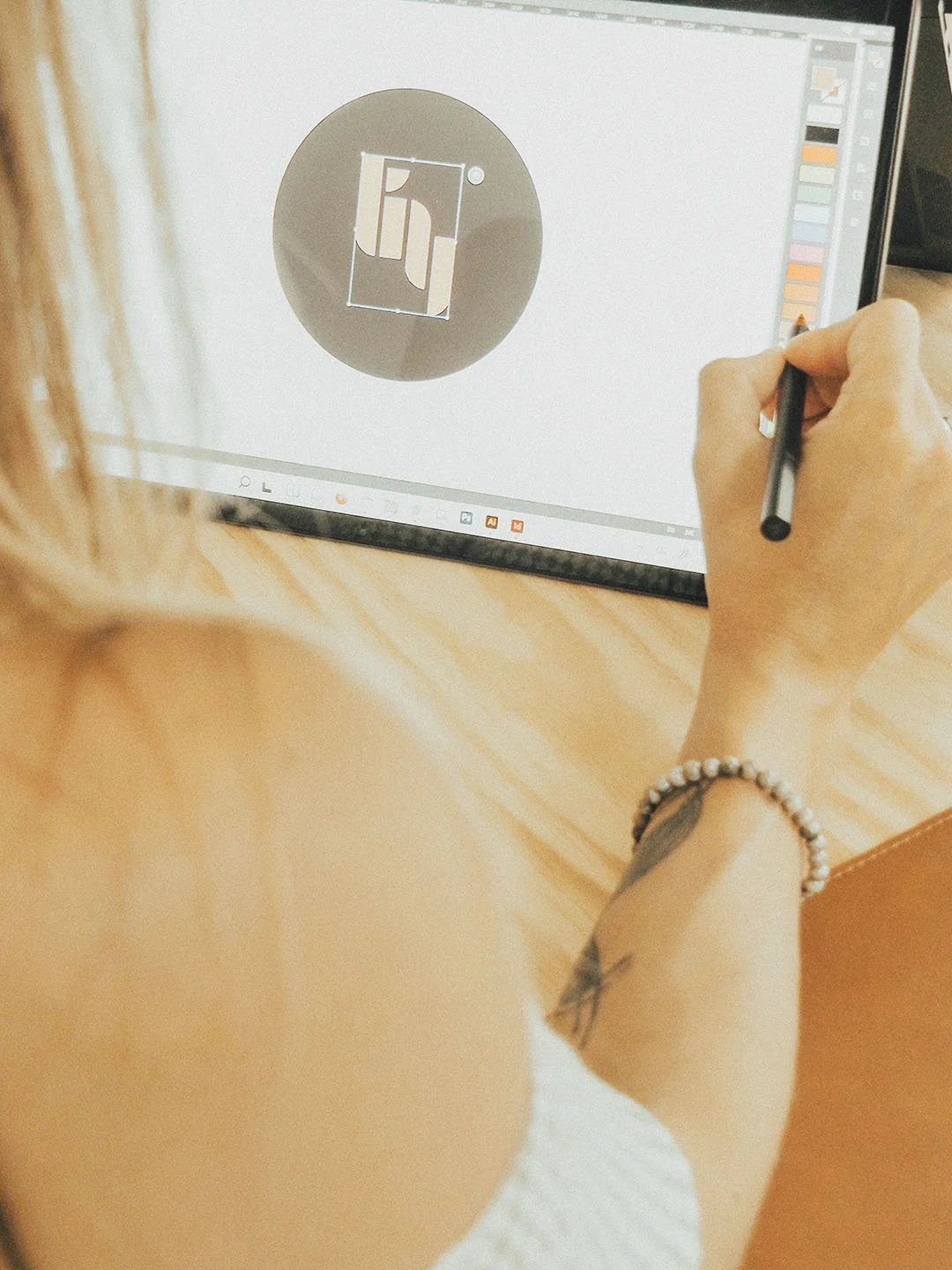 Person designing a logo on a graphic tablet, with a digital drawing program open on the screen showing a black and beige abstract logo.